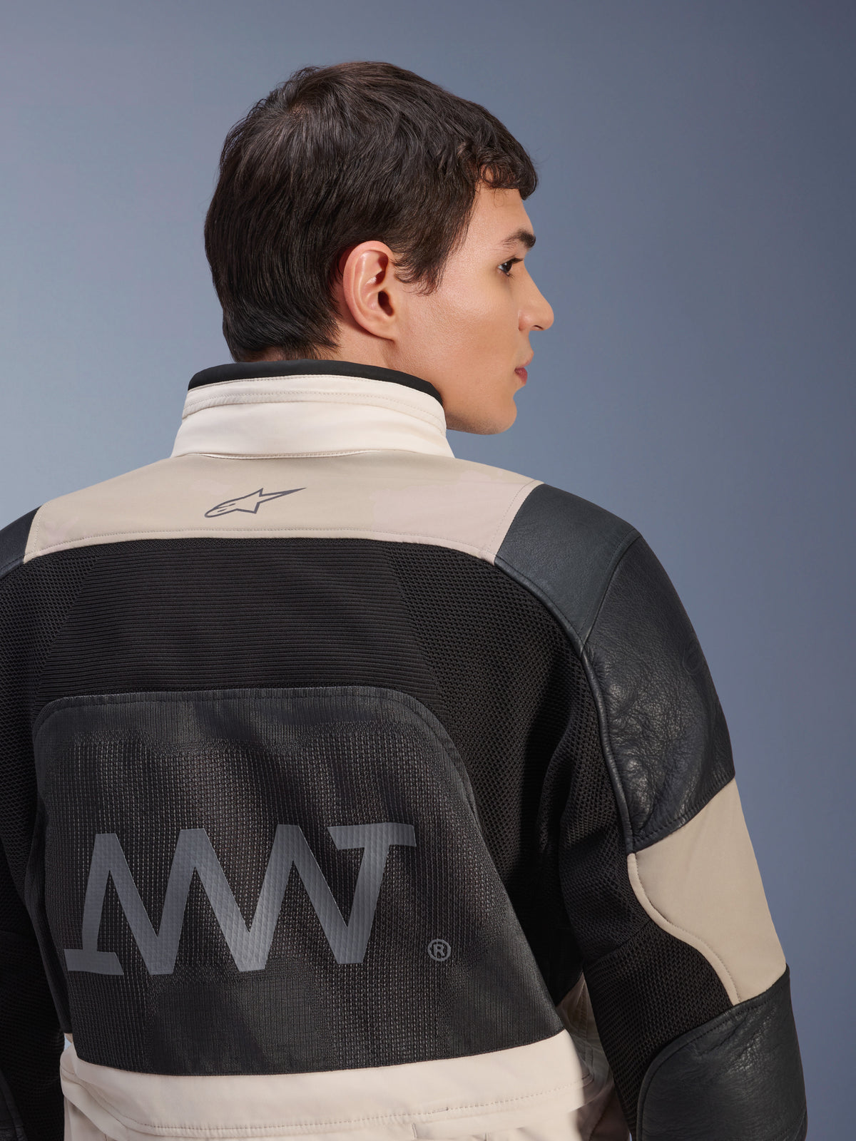 Alpinestars AMT-10LAB Drystar® XF jas, achteraanzicht op mannelijk model, kleurstelling White Sand Aluminum Camo en zwart, met grote AMT-branding, mesh ventilatiepanelen en lederen verstevigingen, technische adventure motorkleding