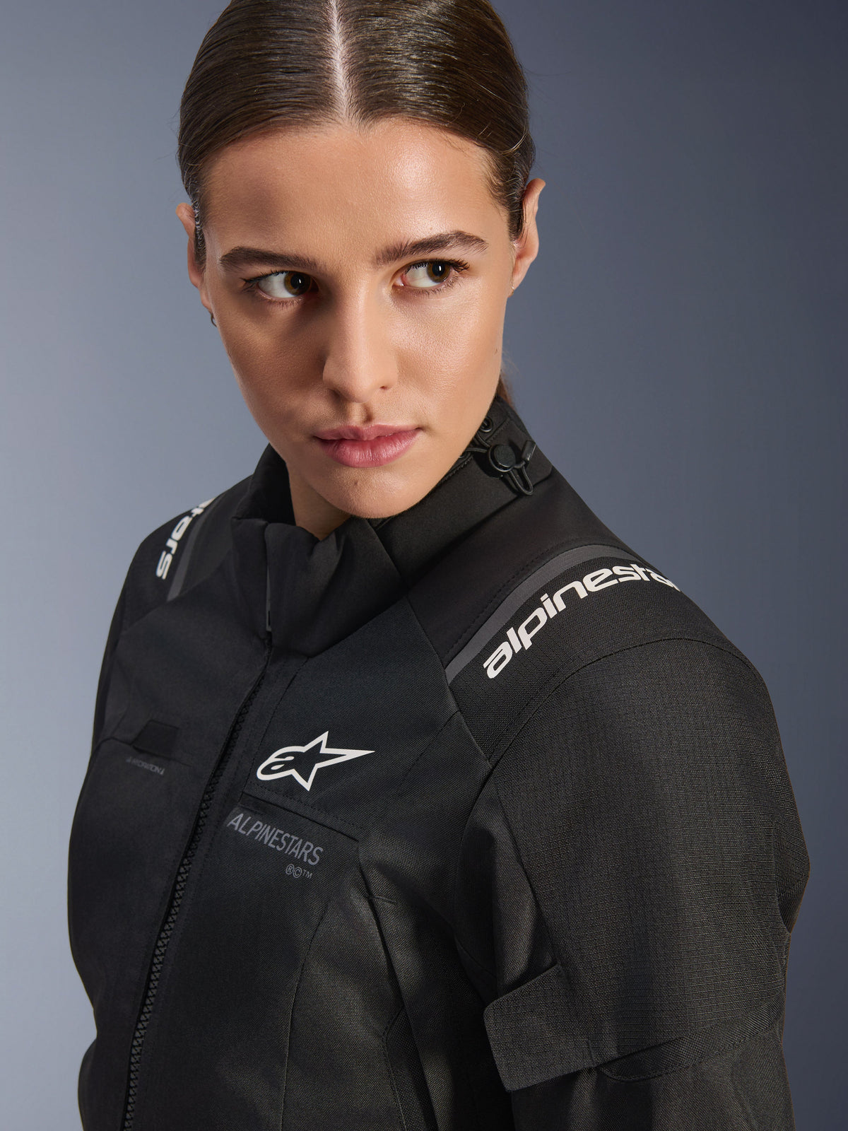Alpinestars Stella Andes V4 Drystar® damesmotorjas, zwarte motorjas, close-up studioportret van het bovenlichaam en de schouder, met witte Alpinestars-logo's, hoogwaardig textielmateriaal en een slanke, vrouwelijke pasvorm