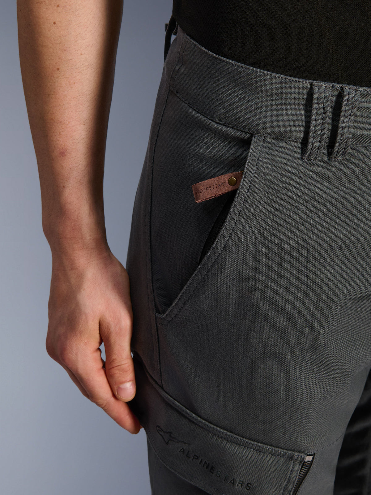 Alpinestars Borrego Drystar® broek, adventure motorbroek, antracietgrijs, close-up detail van de zak en heup, gewaxte canvas textuur met een bruin leren merklabel en geborduurde Alpinestars-branding op de dijzak.