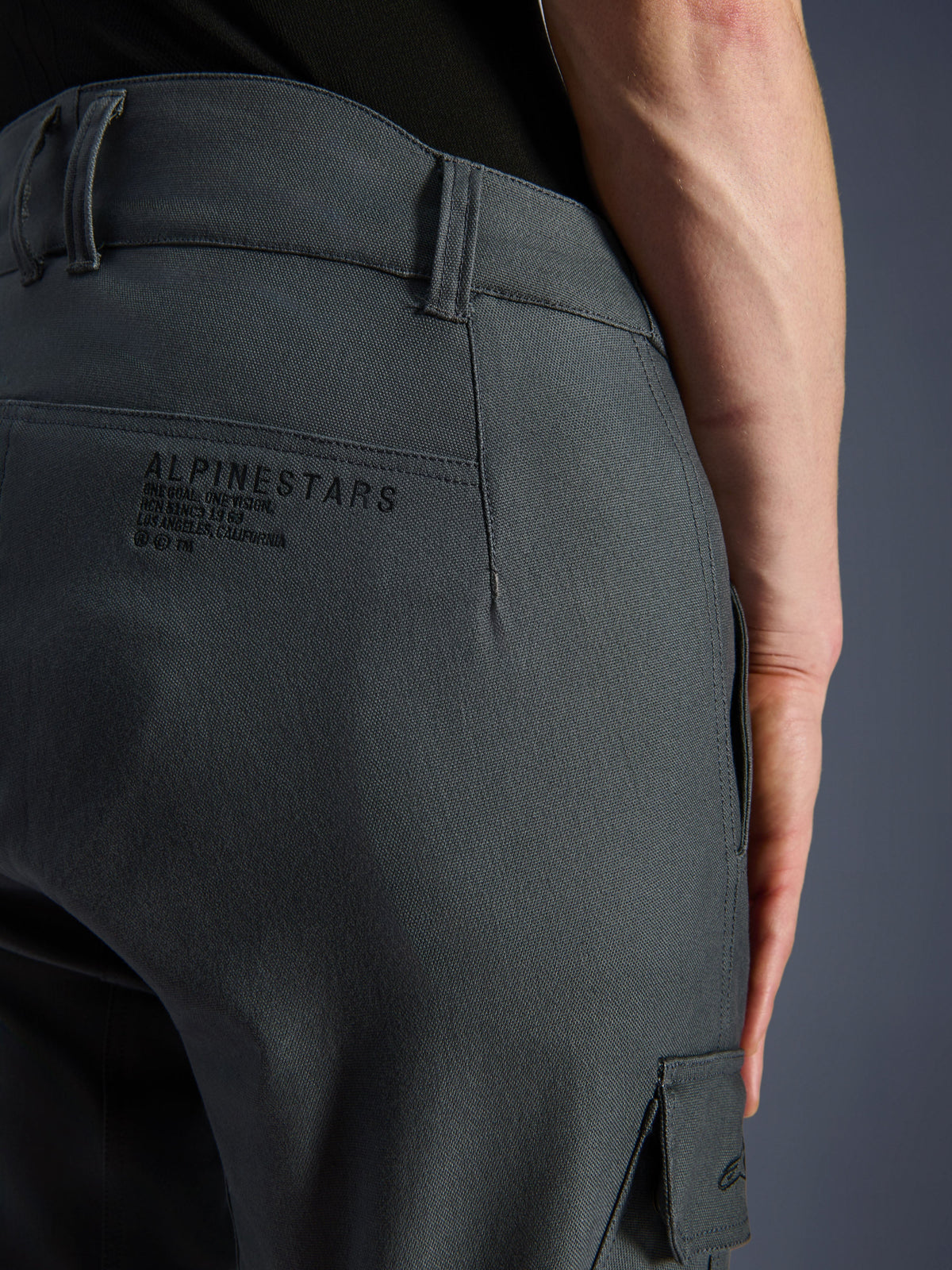 Alpinestars Borrego Drystar® broek, motorbroek, antracietgrijs, close-up van de heup aan de achterkant met Alpinestars branding en slogan, duurzaam textiel met een gewaxte canvas look, adventure motorkleding