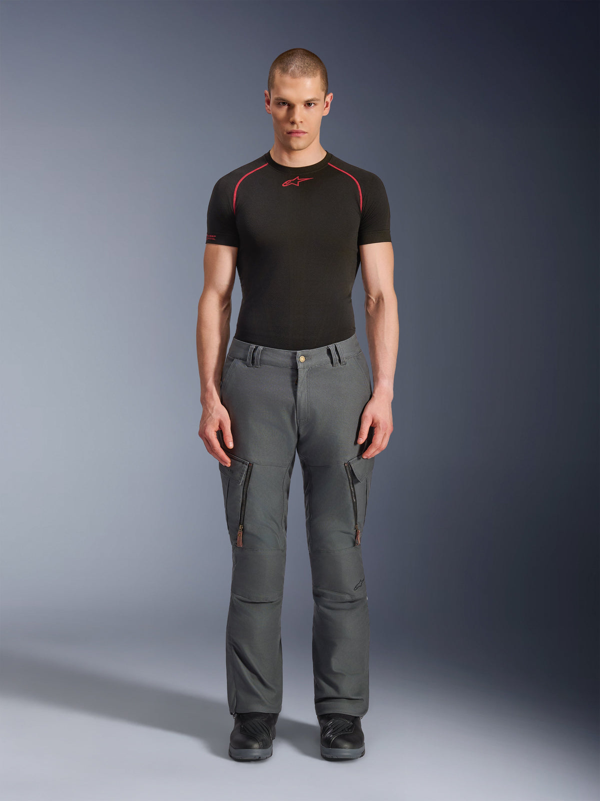 Alpinestars Borrego Drystar® broek, grijze adventure motorbroek, gedragen door een model met een zwart en rood technisch T-shirt en zwarte laarzen, voorzien van cargozakken met verticale ritsen, robuuste gewaxte canvas uitstraling, duurzaam ontwerp voor adventure touring en ritten op de weg