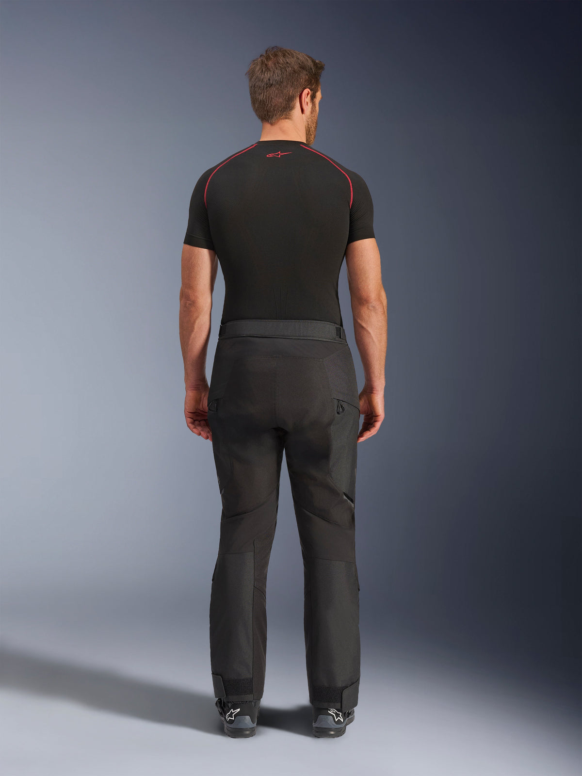 Rijder draagt Alpinestars Cusco Drystar® broek, zwarte adventure motorbroek, achteraanzicht, gecombineerd met een zwart compressieshirt met korte mouwen en zwarte motorlaarzen, voorzien van een duurzaam textielontwerp met voorgevormde panelen voor touring