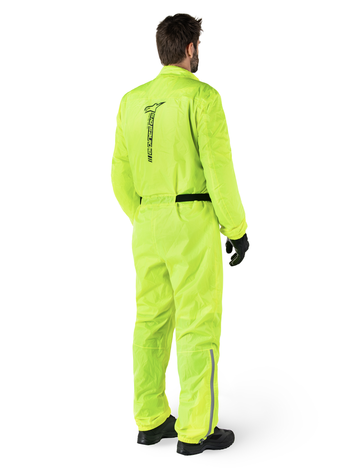 Alpinestars Hurricane Rain V2-pak, Yellow Fluo, achteraanzicht van een rijder die een eendelig motorregenpak draagt, met een zwart Alpinestars-logo op de rug, een zwarte tailleband en reflecterende strips op de onderbenen, gedragen met zwarte handschoenen en laarzen