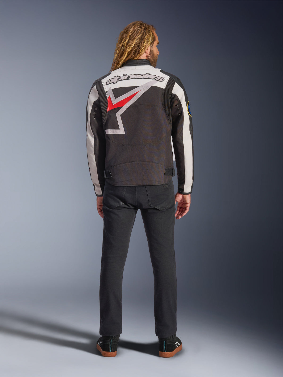 Alpinestars Axton Jacket, motorjas, zwart, off-white en felrood, achteraanzicht op een model, met een groot Alpinestars sterlogo op de rug, off-white mouwpanelen, gedragen met een zwarte broek, vintage-geïnspireerd racing teamwear ontwerp