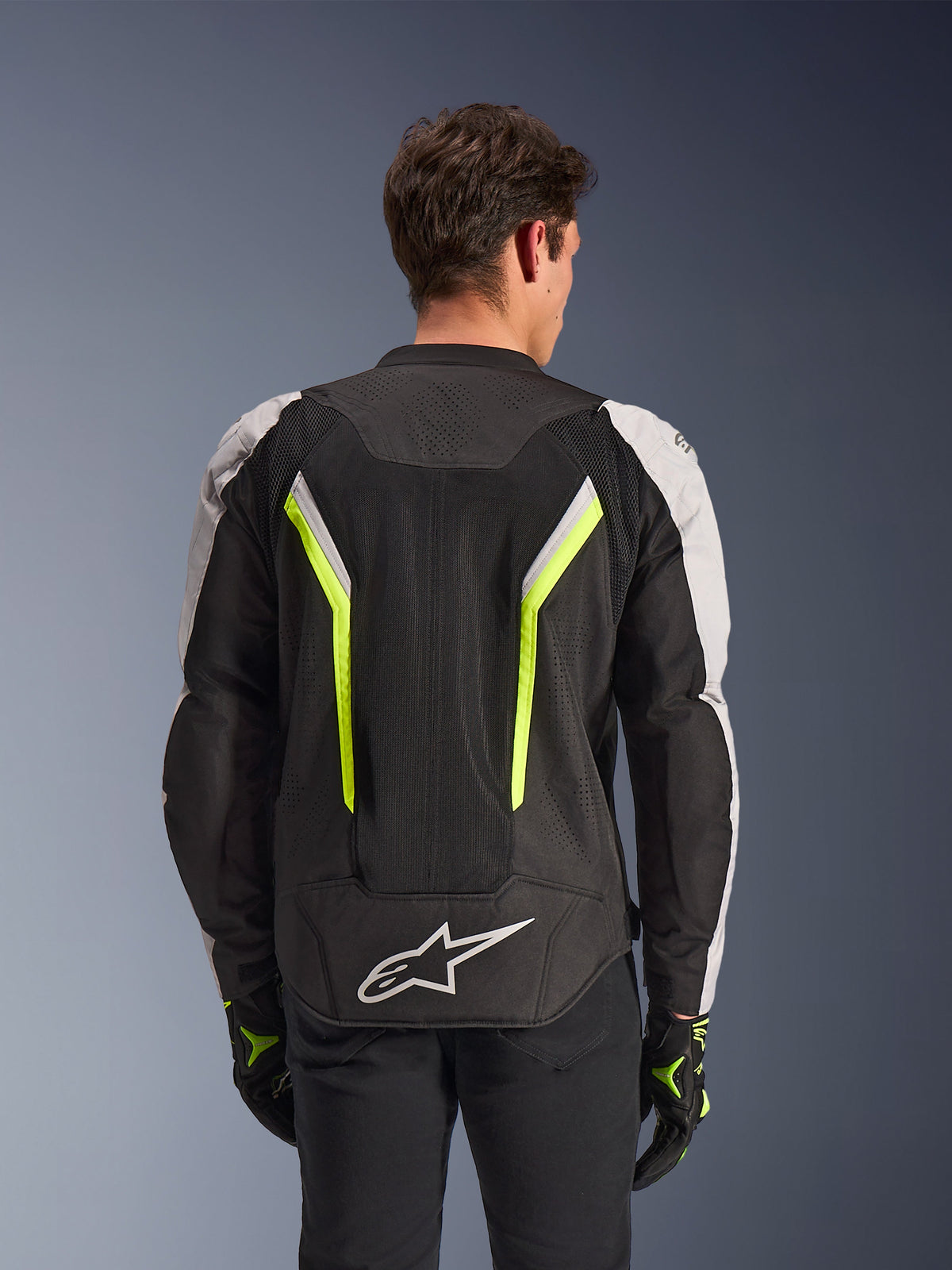 Alpinestars AST V3 Air Jacket, motorjas, zwart zilver en fluorgeel, achteraanzicht op model, textiele jas met dubbele tech mesh ventilatiepanelen, verticale neongele strepen, zilveren mouwen en wit Alpinestars-logo op de onderrug.