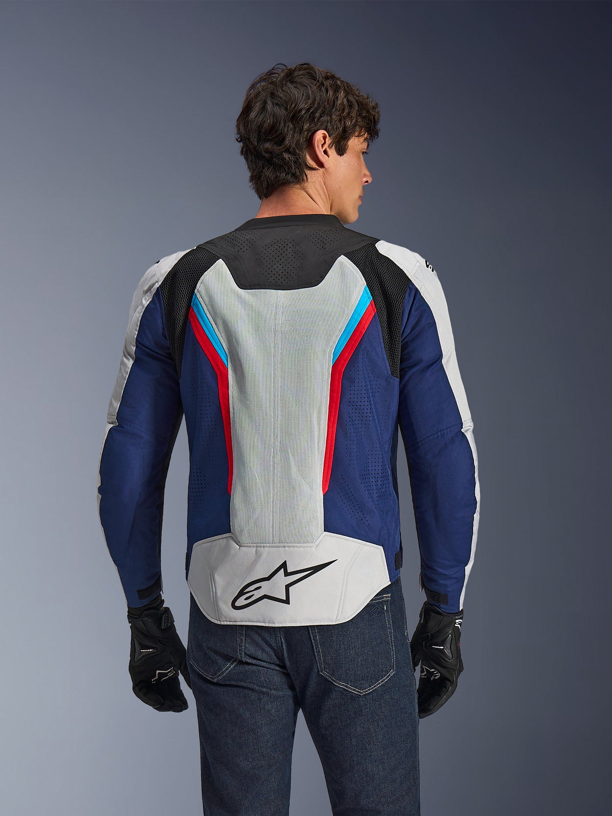 Alpinestars AST V3 Air Jacket, motorjas, Silver Deep Blue Bright Red, achteraanzicht gedragen door een rijder, voorzien van tech mesh-panelen en laserperforaties voor ventilatie, zwart sterlogo op de onderrug, sport-geoptimaliseerd ontwerp voor warm weer