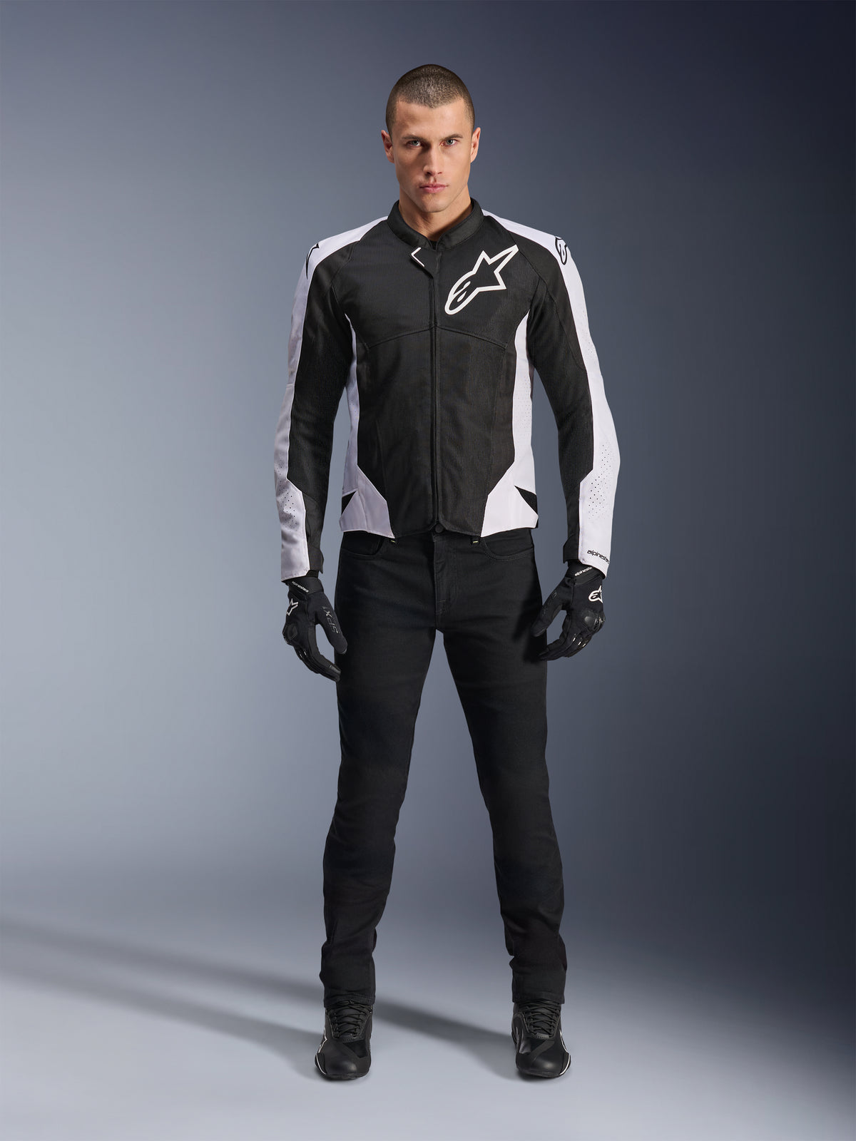 Alpinestars Viper Air V4 Jas, zwart-witte motorjas met groot wit logo op de borst, gedragen door een mannelijk model met zwarte broek en handschoenen, voorzien van meshpanelen voor ventilatie, sportieve motorkleding voor op de weg