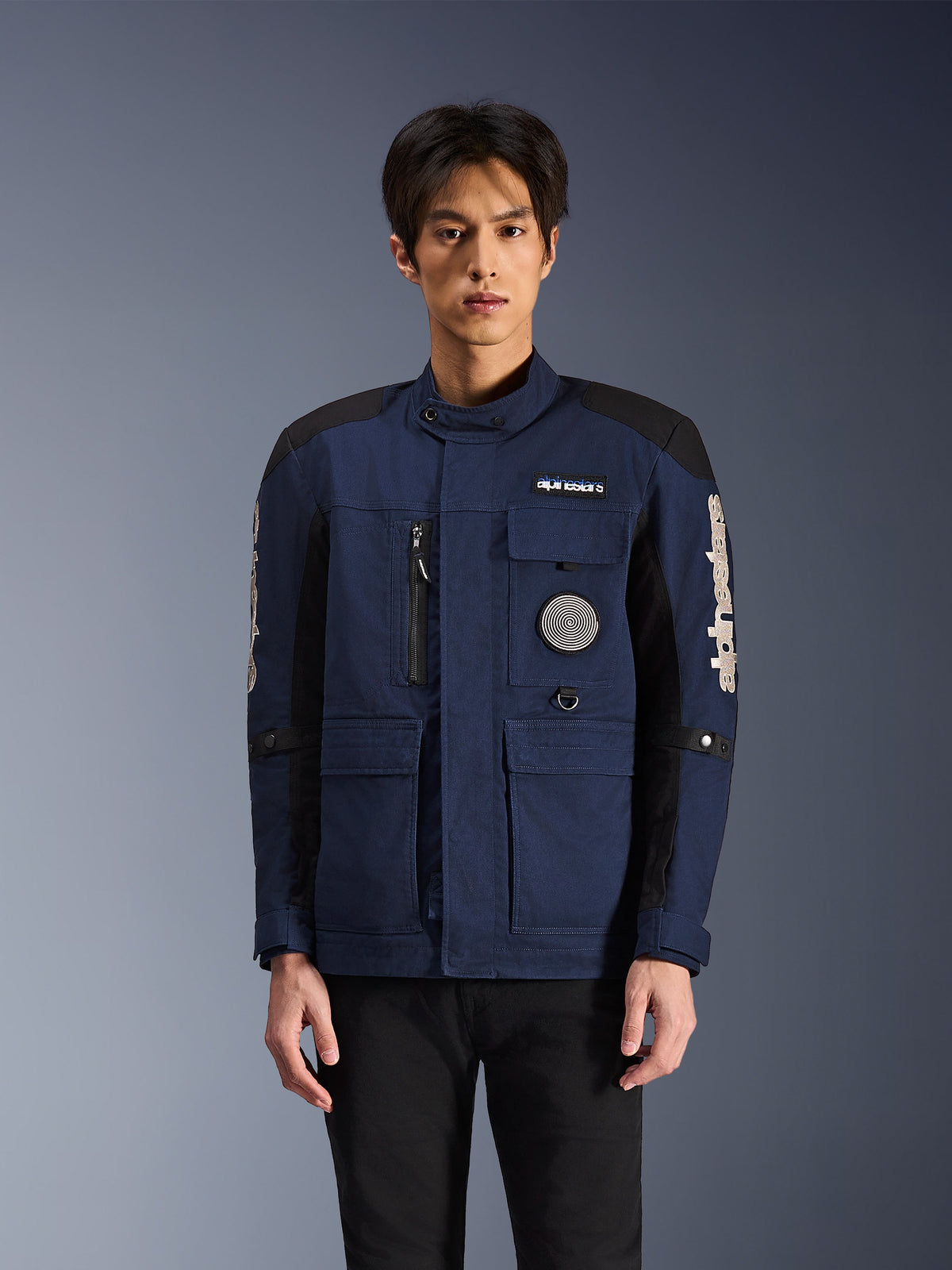 Alpinestars Dice Jacket, stedelijke motorjas, donkerblauw en zwart, veldjas-ontwerp met meerdere zakken, spiraalvormige patch op de borst en witte Alpinestars-branding op de mouwen, moderne op werkkleding geïnspireerde motorkleding