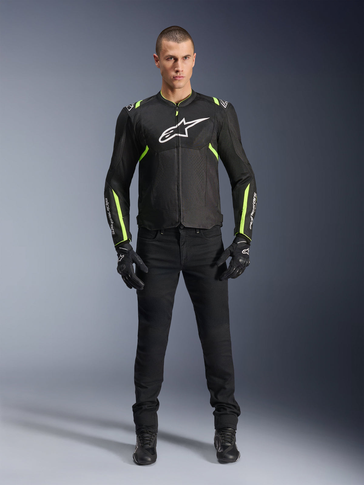 Alpinestars T-Sps Air V2 Jas, Zwart en Geel Fluo, textiele motorjas met mesh-panelen, gedragen door mannelijk model met zwarte broek en handschoenen, voorzien van wit Alpinestars-logo op de borst, urban sport motorkleding