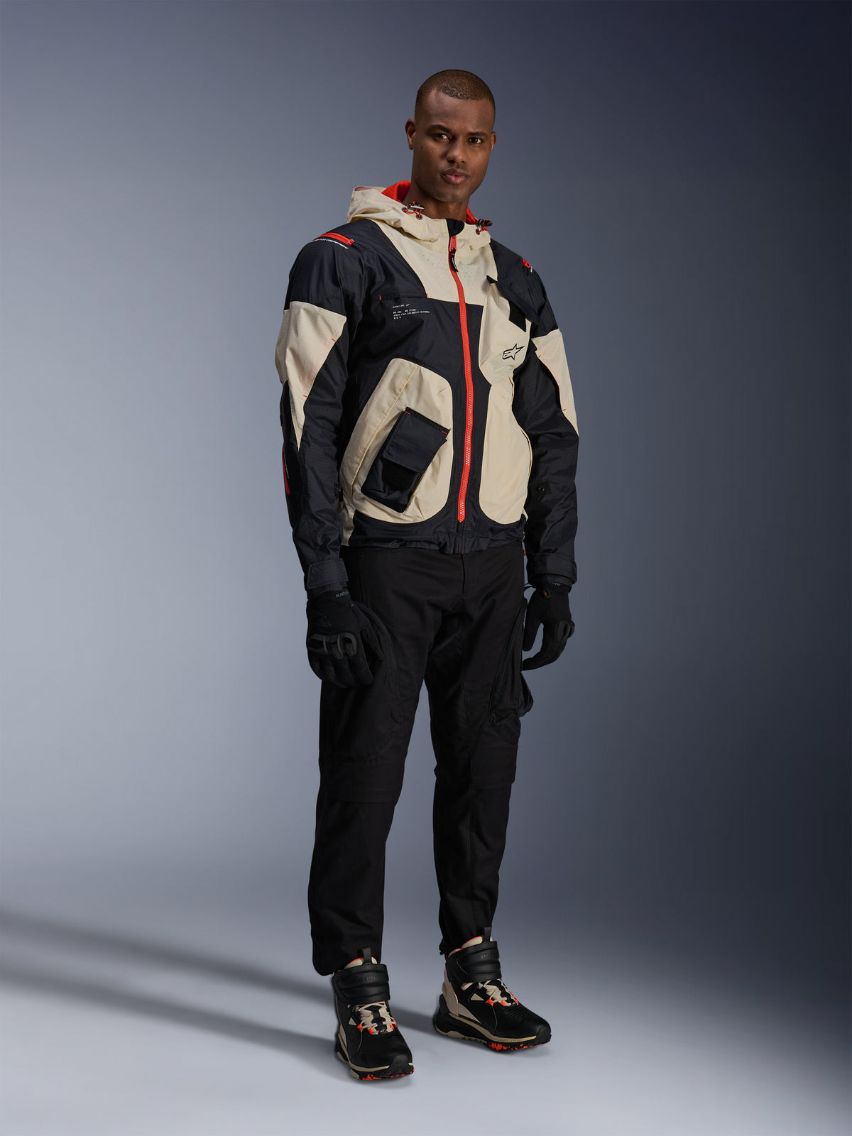 Alpinestars Acteon broek, zwarte motorbroek, gedragen met een zwart, beige en rood Mogress Air Jacket, zwarte motorhandschoenen en bijpassende hoge motorsneakers, eigentijdse urban motoruitrusting voor heren