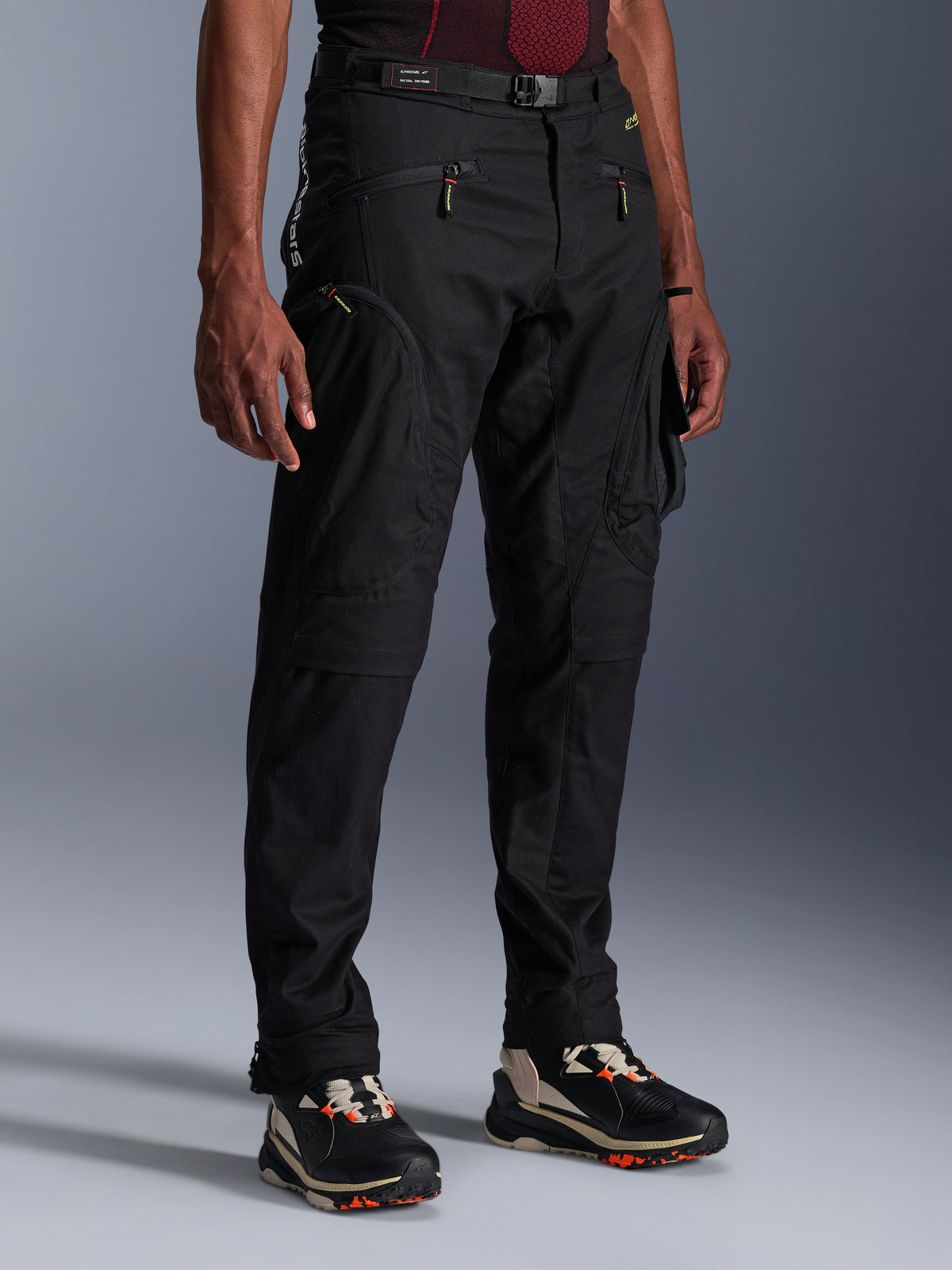Alpinestars Acteon broek, zwarte motorbroek, gedragen door een model, met een modern taps toelopend silhouet, cargozakken met ritssluiting, verstelbare tailleriem en technische sneakers, stedelijke motorkleding