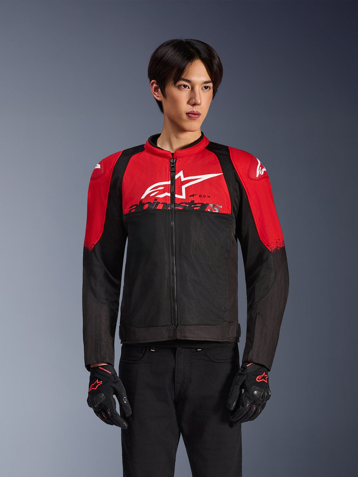 Alpinestars SMX Air Jacket, mesh motorjas, felrood en zwart, gedragen door een model met zwarte motorhandschoenen, voorzien van een groot wit logo op de borst, geventileerde textielconstructie met rode schouderpanelen en zwarte mouwen, sportieve kleding voor ritten in warm weer