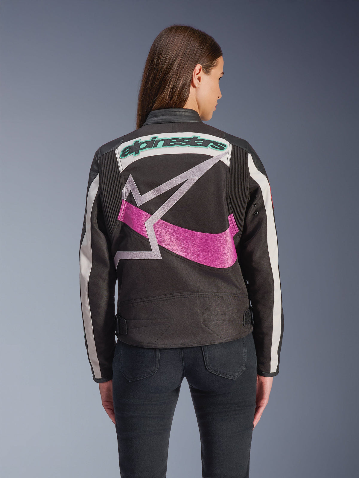 Alpinestars Idles damesjas, achteraanzicht, zwart met gebroken wit en paars, groot grafisch sterlogo op de rug, groenblauw geborduurd woordmerk, accordeonpanelen op de schouders, vintage-geïnspireerde stedelijke motorkleding