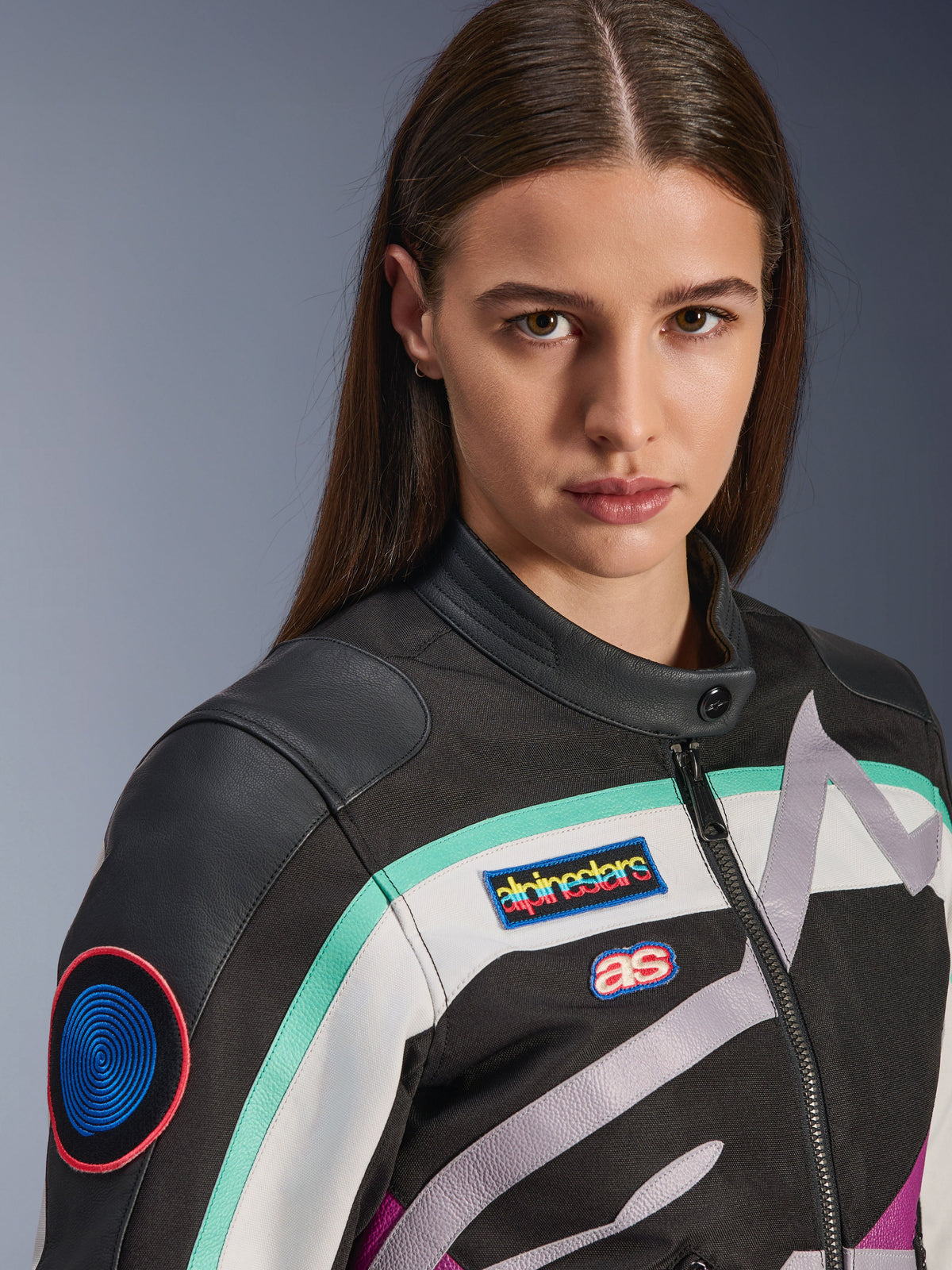 Alpinestars Idles damesjas, motorjas, zwart, gebroken wit en paars met blauwgroene accenten, close-up met kleurrijke Alpinestars heritage patches en geitenlederen schouderdetails, vintage-geïnspireerd ontwerp voor stedelijk rijden.