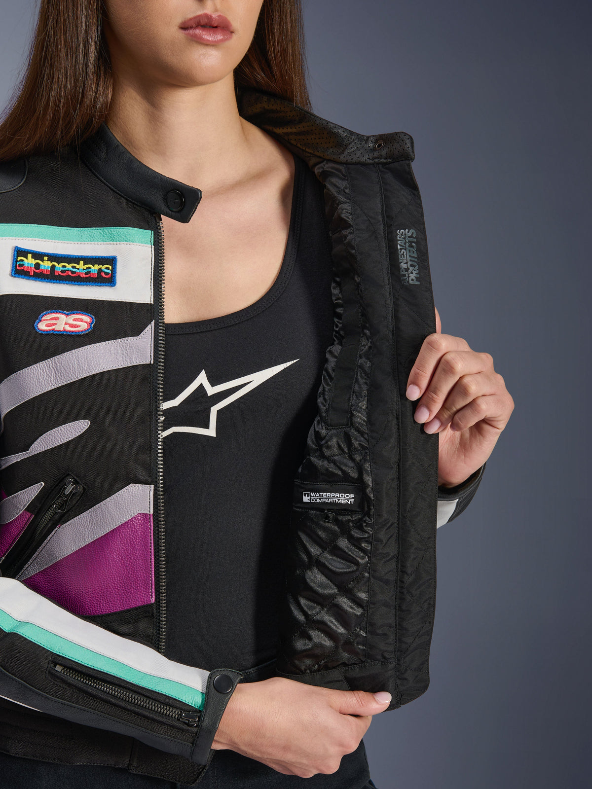 Alpinestars Idles damesjas, Black Off White Purple, close-up van de gewatteerde binnenvoering met waterdicht compartiment, voorzien van vintage race-patches en kleurrijke teal en paarse accenten op de buitenkant van textiel.