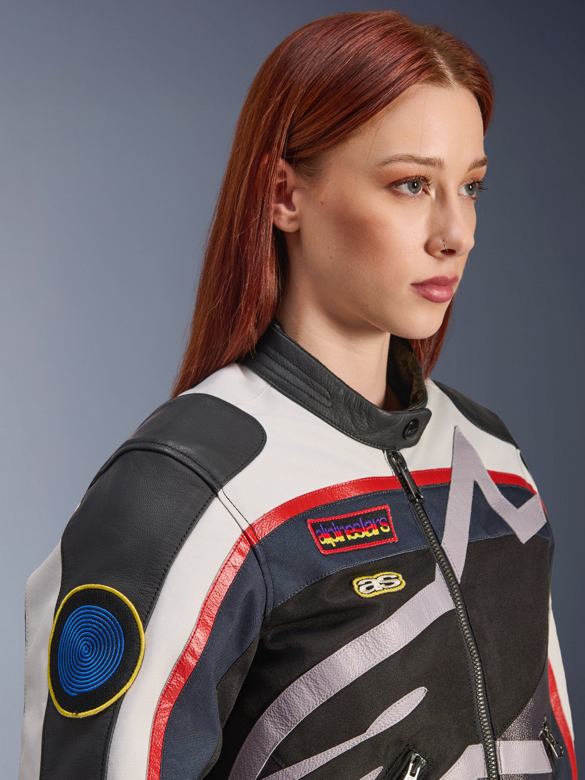 Alpinestars Idles damesjas, Off White, vlamrood en zwart, met vintage-geïnspireerde race-patches en een rondom lopend logo, constructie van textiel en leer, urban motorstijl gedragen door een model.
