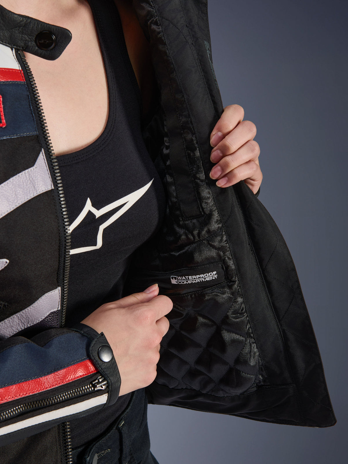 Alpinestars Idles damesjas, interieurdetail met zwarte gewatteerde voering en gelabeld waterdicht compartiment, gedragen over een zwarte tanktop met logo, functionele motorkleding voor dames