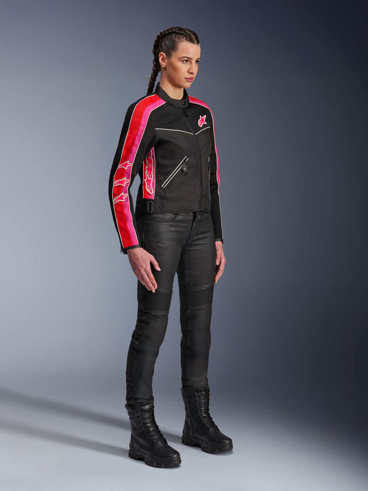 Alpinestars Stella T-Dyno Air Jas, motorjas voor dames, zwart met felrode en fuchsia strepen op de mouwen, gedragen met zwarte motorbroek en laarzen, vintage-geïnspireerd mesh-ontwerp voor urban rijden