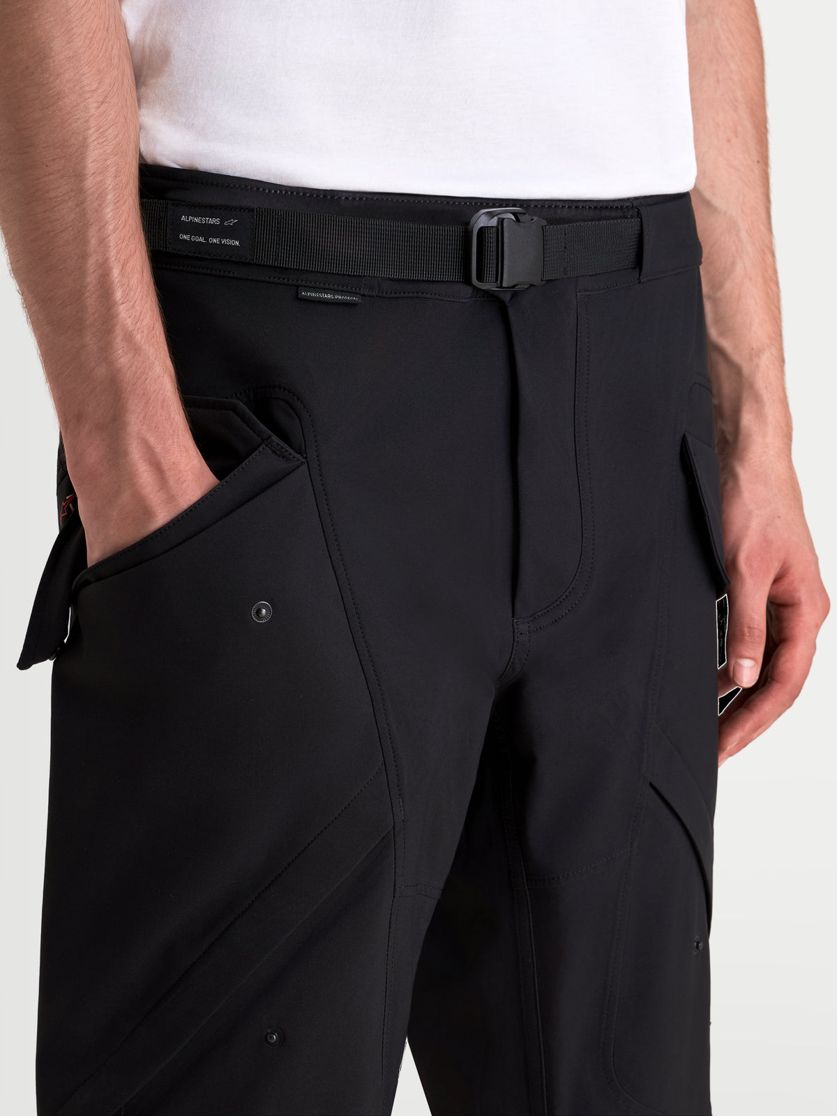 Alpinestars Juggernaut V2 Drystar broek, urban motorbroek in zwart, detailweergave van de verstelbare riem, magnetische gesp en cargozakken aan de voorkant op een model
