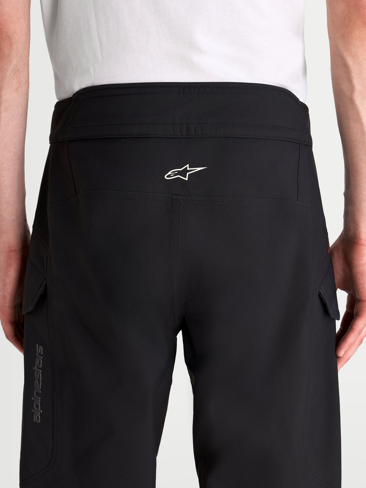 Alpinestars Juggernaut V2 Drystar broek, waterdichte urban motorbroek voor heren in zwart, achteraanzicht met hoge tailleband, wit Astar-logo en cargozakken gedragen door een model