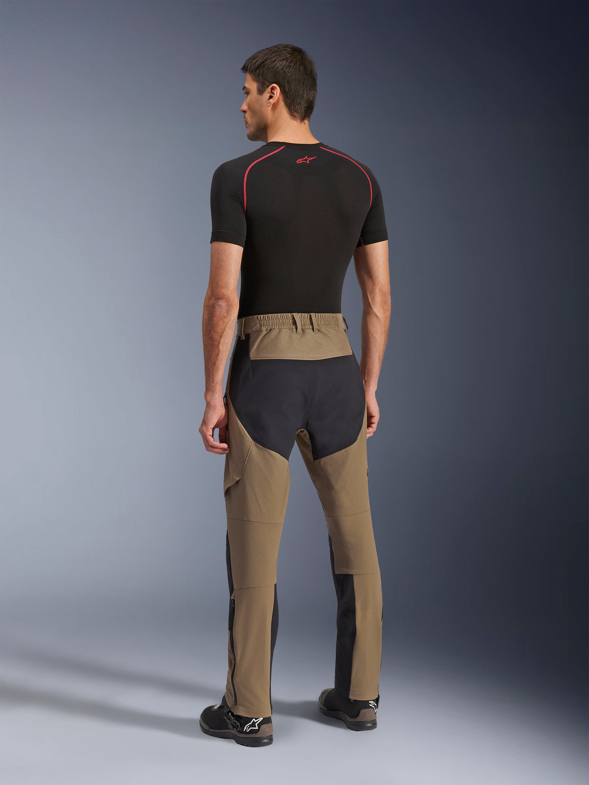 Alpinestars Flex-AST Explorer Broek, adventure motorbroek, Walnut Black, achteraanzicht op model met zwarte ripstop-panelen op het zitvlak en de benen, stretch textielconstructie en lange ritsen aan de onderbenen voor adventure touring