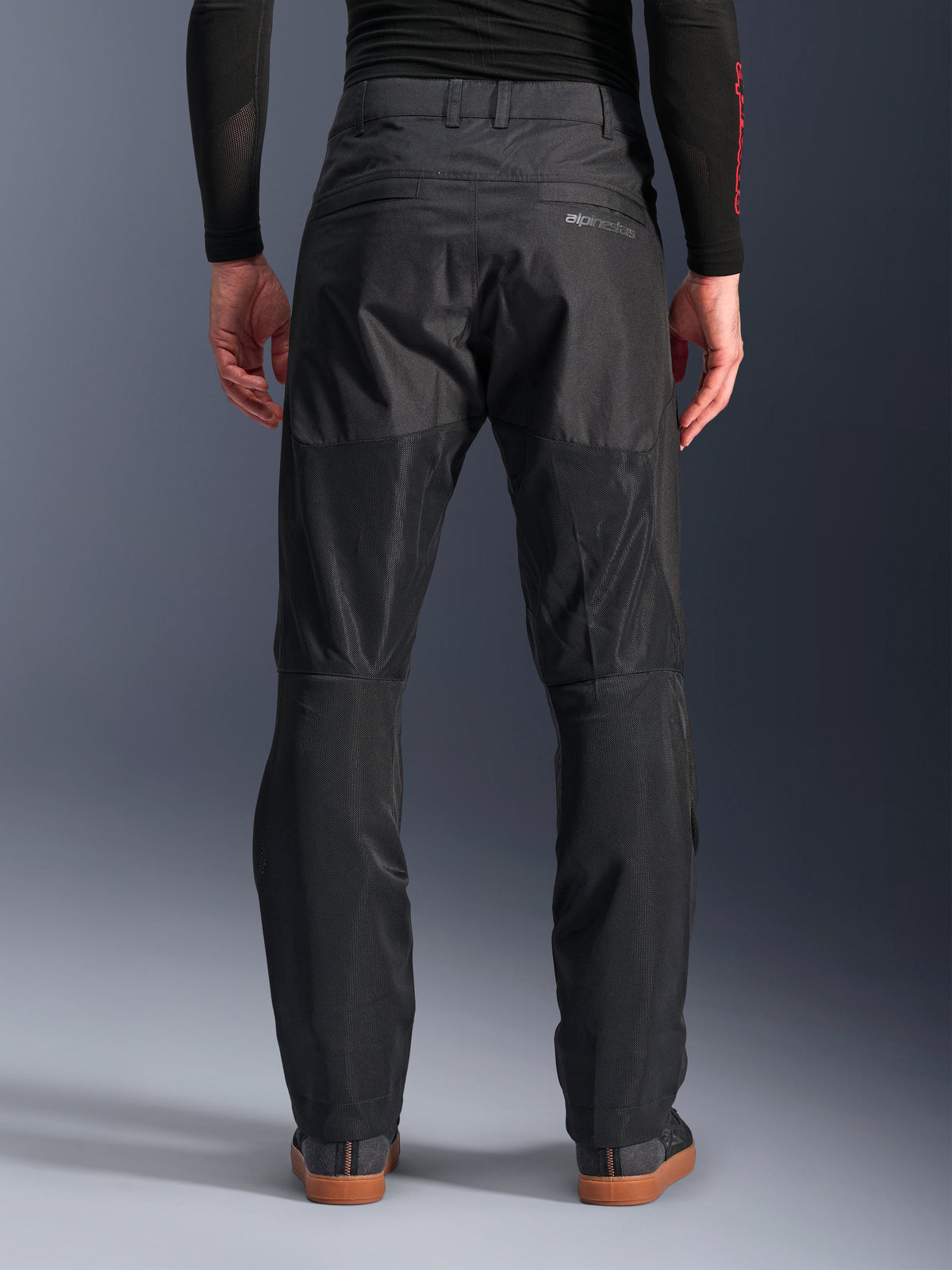 Alpinestars C-1 Air Pants, achteraanzicht, zwart, urban textiele motorbroek met grote tech mesh panelen aan de achterzijde van de benen voor ventilatie, strak ontwerp met subtiele branding, gedragen met een zwarte basislaag en casual motorschoenen.