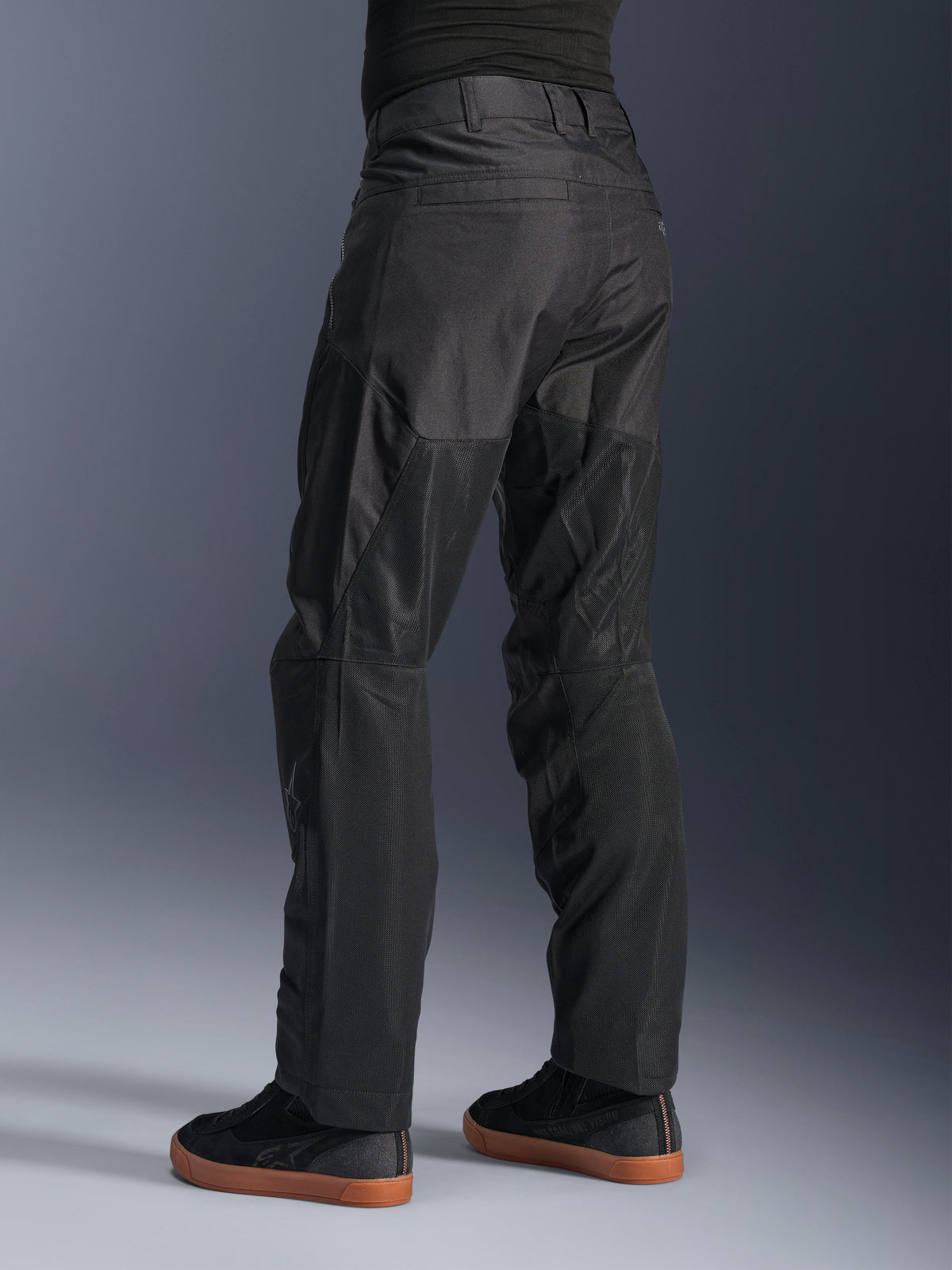 Alpinestars C-1 Air broek, stedelijke motorbroek, zwart, achteraanzicht met grote tech mesh-panelen aan de achterkant van de benen voor ventilatie, strakke styling voor stadsritten, gedragen met casual zwarte sneakers