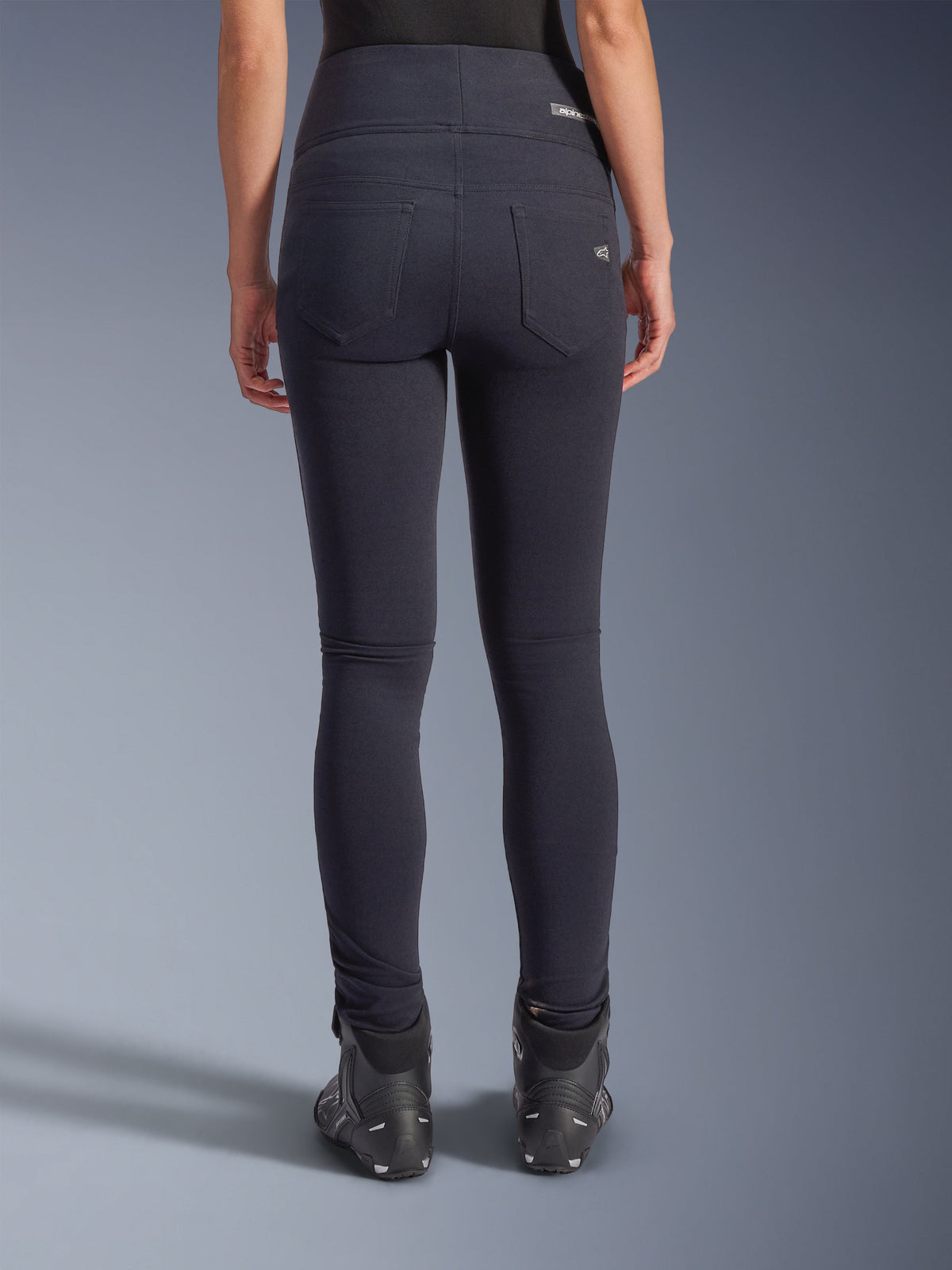 Alpinestars Stella Flex-AST Leggings, urban motorbroek, zwart, achteraanzicht met skinny pasvorm en hoge taille, twee functionele achterzakken met subtiele branding, stretch textielmateriaal, gedragen met zwarte motorschoenen
