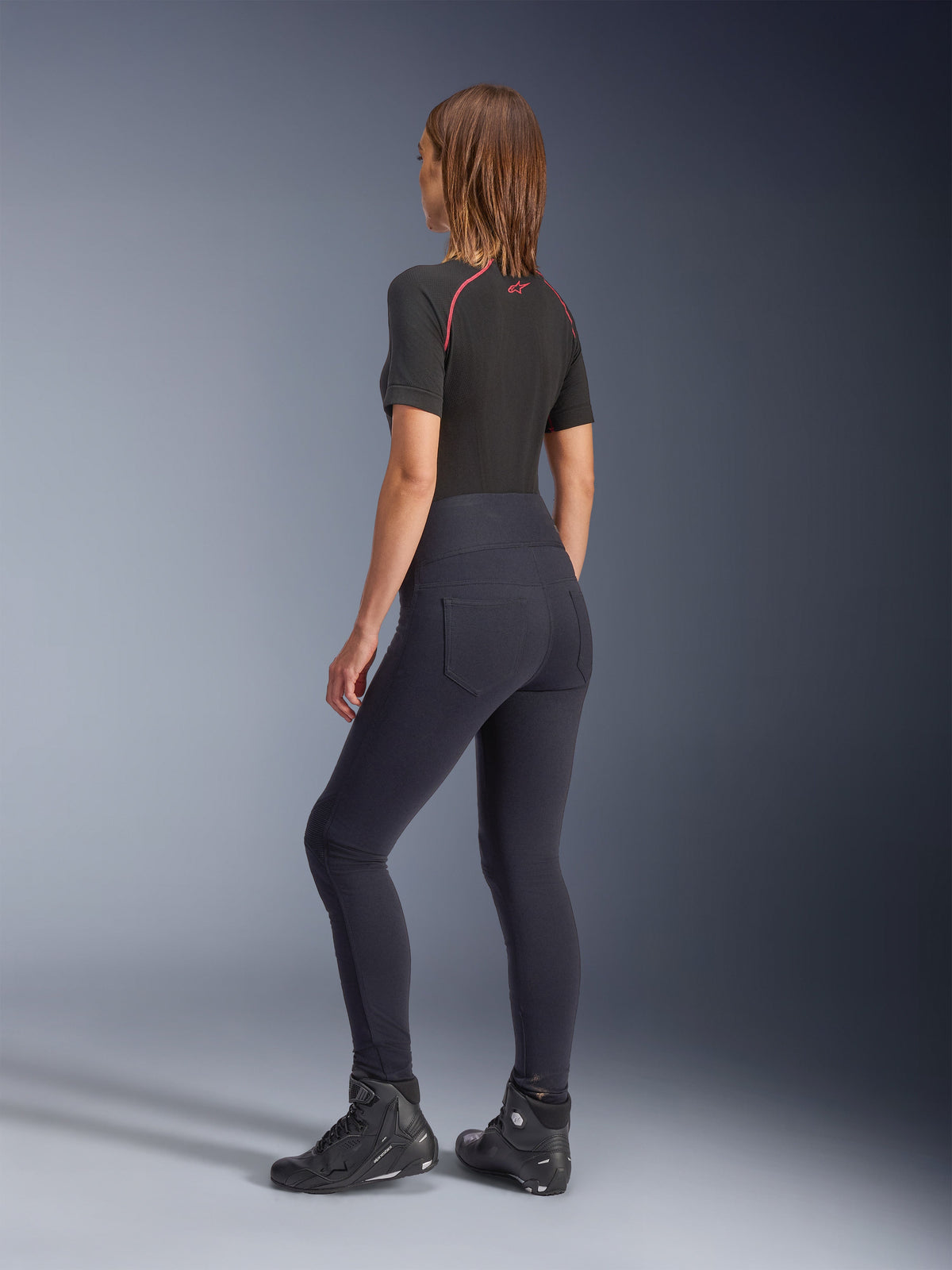 Alpinestars Stella Flex-AST Leggings voor dames, zwarte motorlegging met hoge taille, achteraanzicht met skinny pasvorm en achterzakken, gedragen met zwarte top met korte mouwen en motorlaarzen, urban motorkleding voor dames