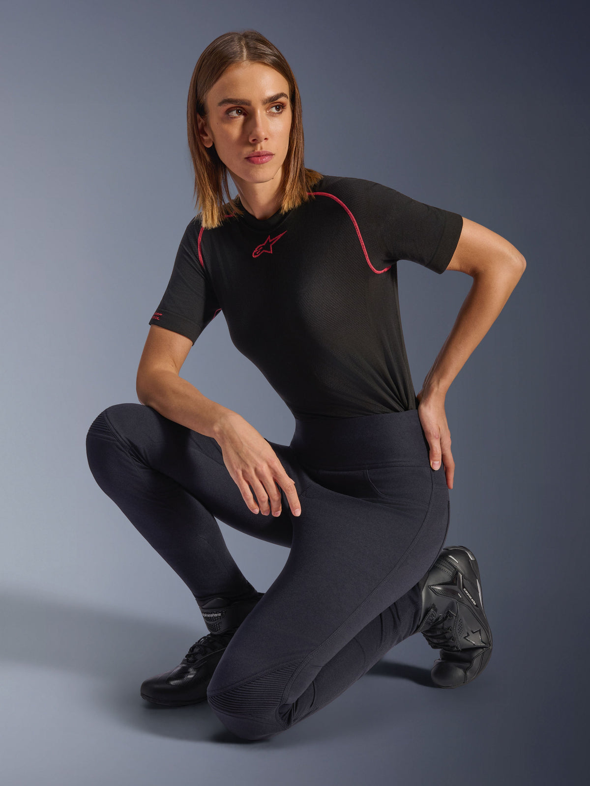 Vrouw in Alpinestars Stella Flex-AST Leggings, zwarte skinny motorlegging met hoge taille en harmonicavormige kniepanelen, gestyled met een zwart performance T-shirt met roze stiksels en motorlaarzen