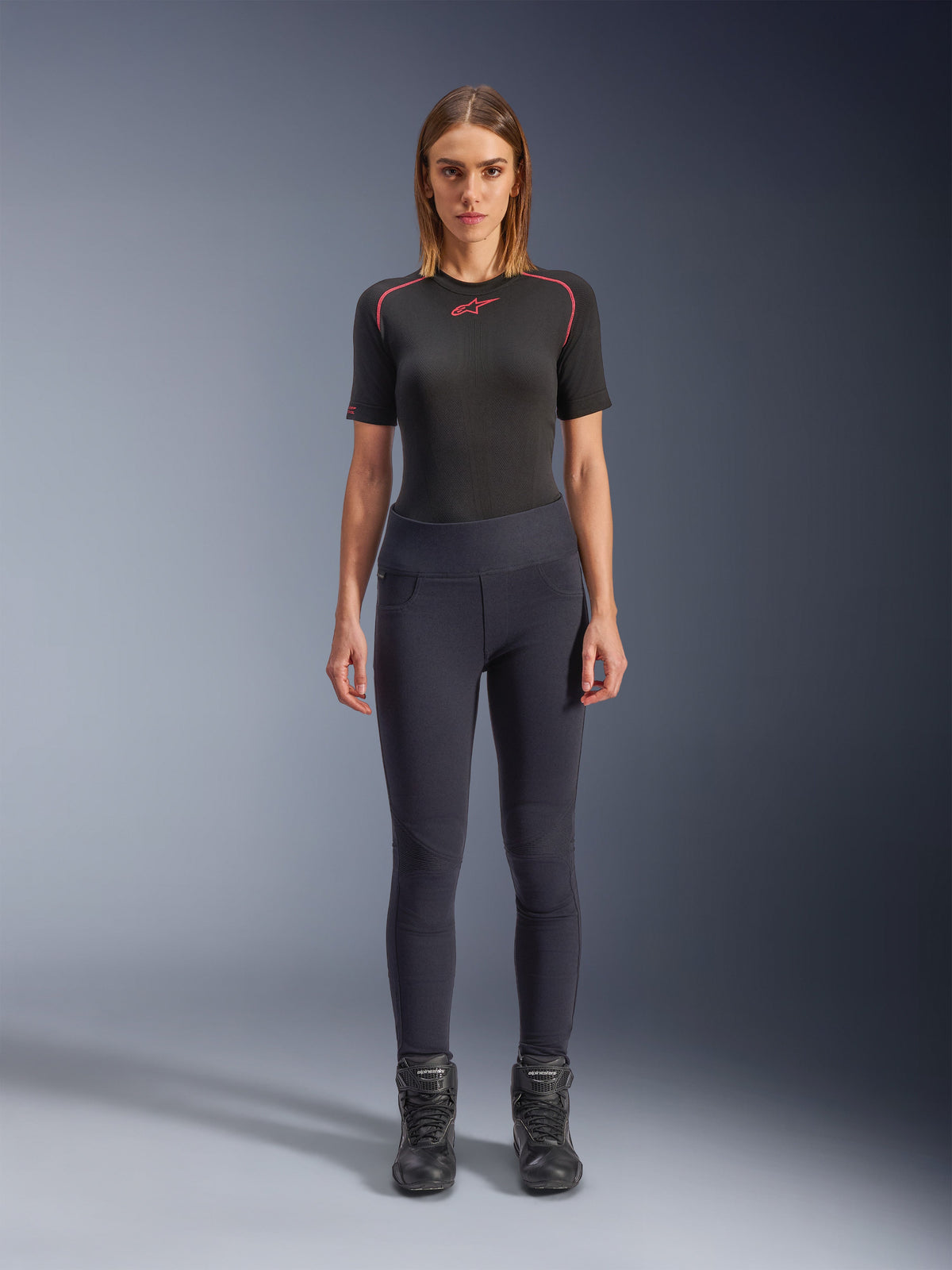 Alpinestars Stella Flex-AST Leggings, stedelijke motorleggings voor dames in het zwart, skinny model met hoge taille, gedragen met een zwart technisch shirt met korte mouwen en zwarte motorlaarzen, voorzien van harmonicavormige kniepanelen en een eigentijdse minimalistische look