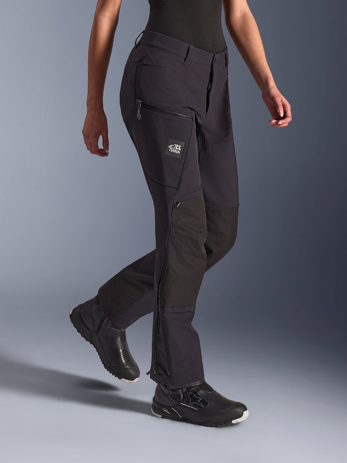 Alpinestars Stella Flex-AST Explorer damesmotorbroek, zwart, adventure motorbroek met stretch textielconstructie en ripstop knieversterkingen, cargozakken met ritssluiting en TERRA-branding, en ritsen aan de onderbenen, gedragen met zwart motorschoeisel.