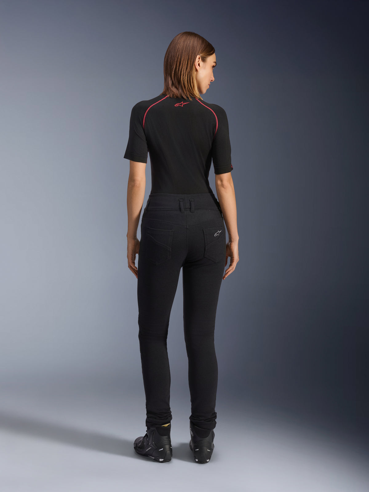Alpinestars Banshee damesleggings, zwarte motorlegging, achteraanzicht met nauwsluitende pasvorm en anatomische stretchstof, voorzien van achterzakken en logodetails, gedragen met een zwarte base layer en motorschoenen, urban motorkleding voor dames