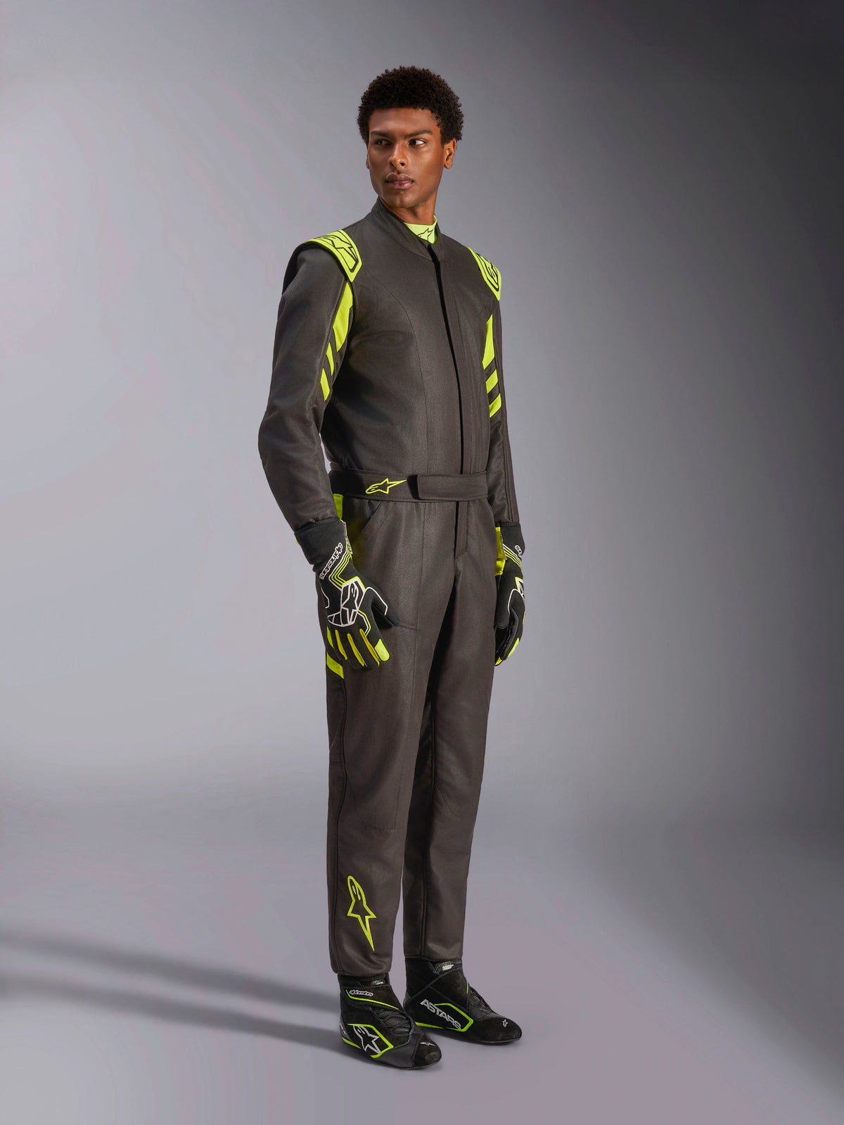 Alpinestars GP Race V3 Suit FIA, autoracepak, zwart met fluoriserend geel, gedragen door een model met bijpassende racehandschoenen en laarzen, voorzien van opvallende gele accenten op de schouders en benen, professionele motorsportuitrusting