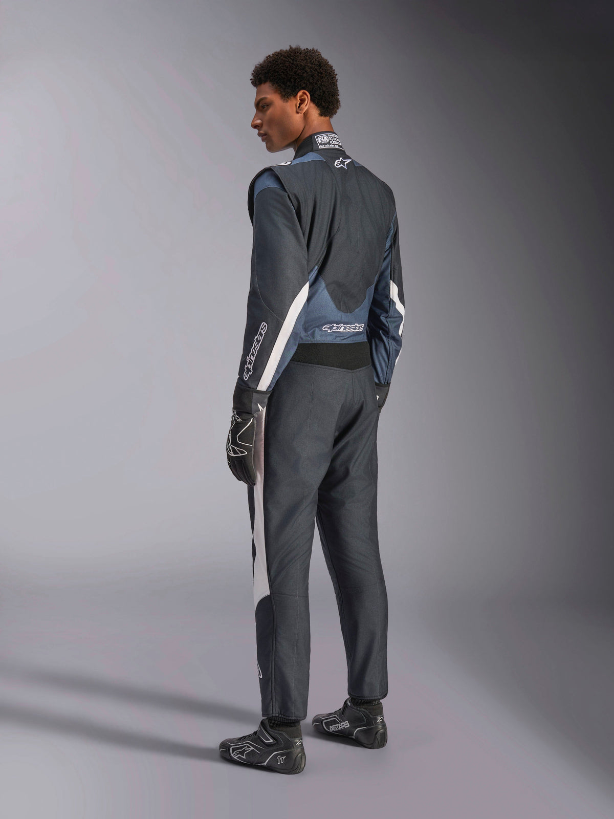 Alpinestars GP Pro Comp V2 FIA pak, heren autoracepak in zwart en asfalt met witte accenten, driekwart achteraanzicht.