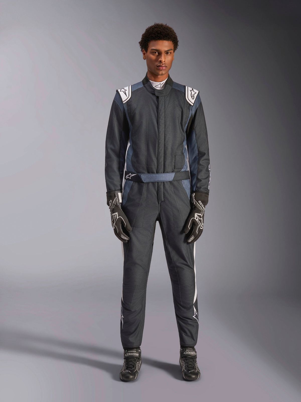 Alpinestars GP Pro Comp V2 FIA pak, heren racepak voor circuitrijden, zwart, asfalt en wit, vuurbestendig, gedragen door een model met bijpassende handschoenen.
