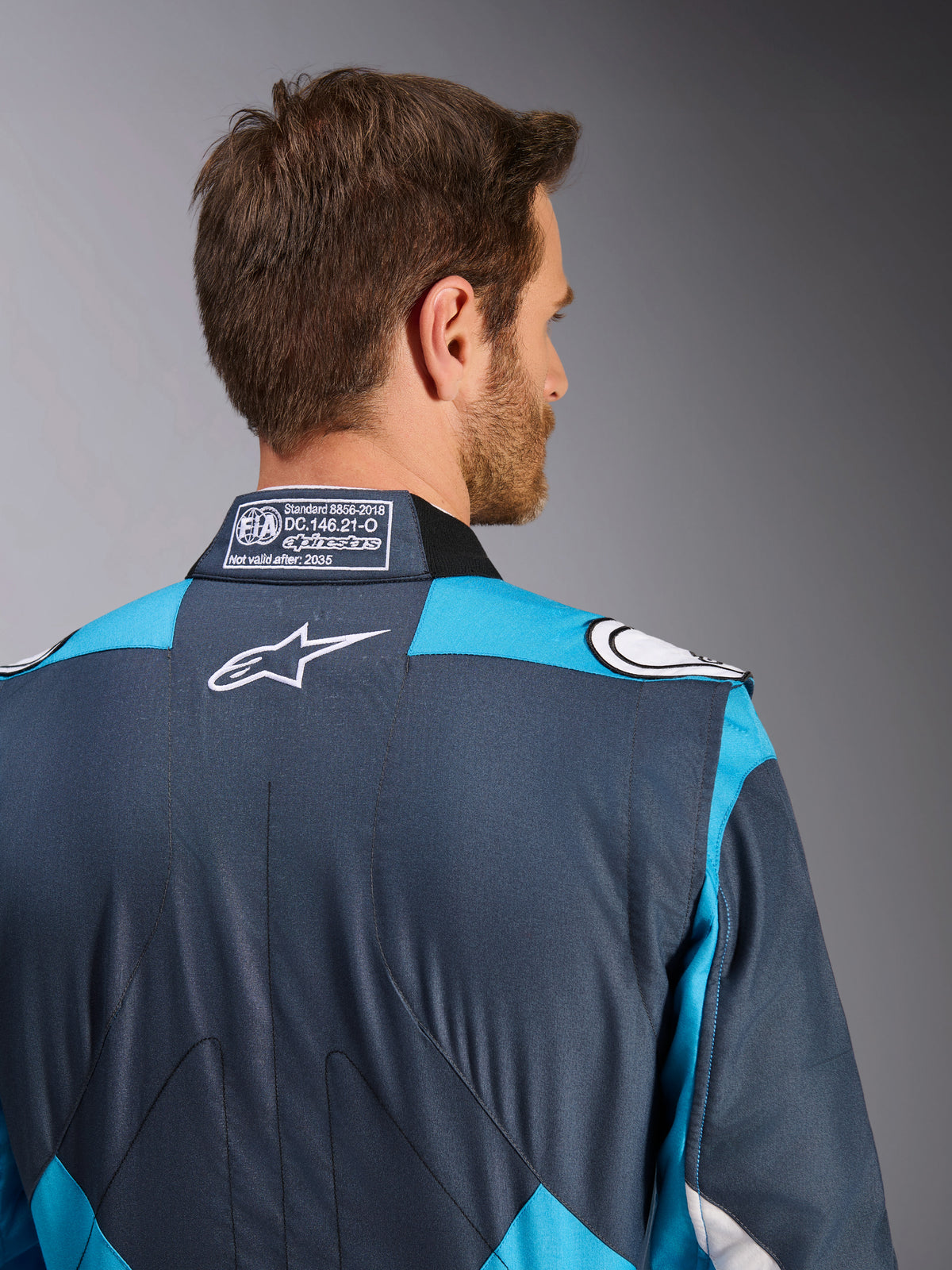 Alpinestars GP Pro Comp V2 Pak - FIA, heren-autoracepak, asfalt en cyaan, wit logo en FIA-homologatielabel op de kraag.