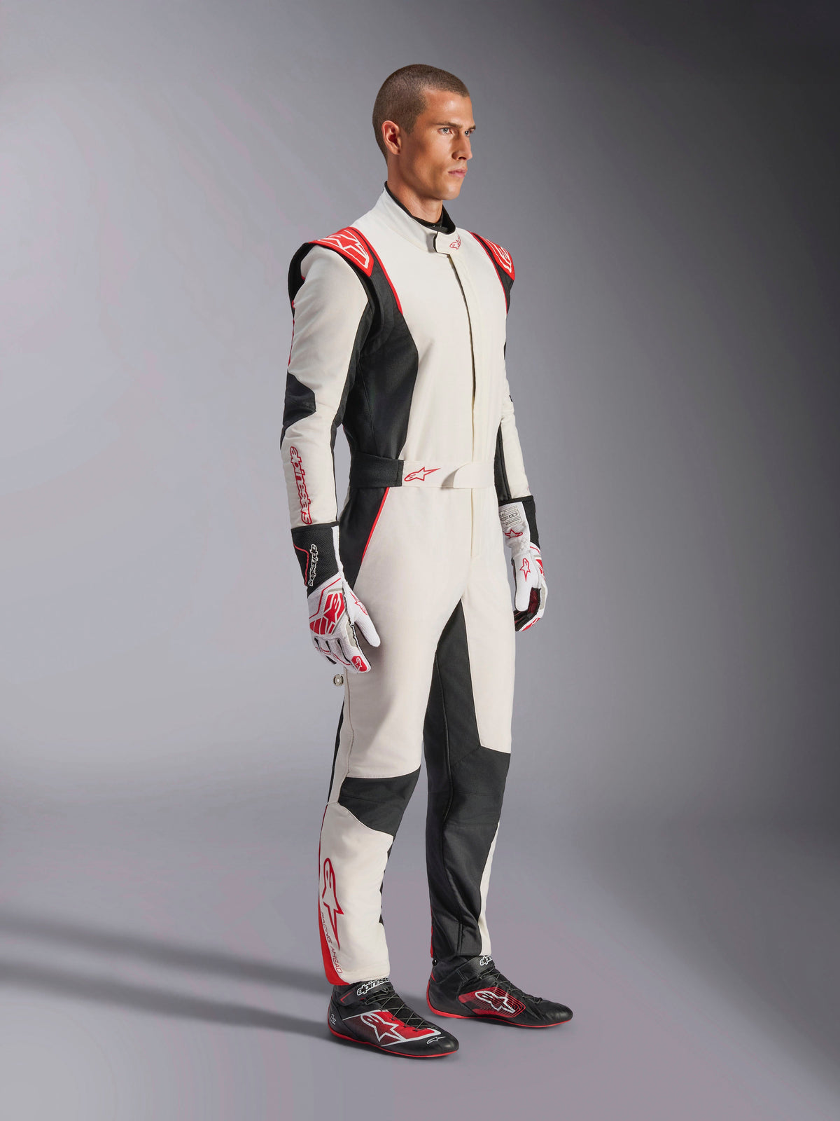 Mannelijke coureur draagt Alpinestars GP Tech V4-pak, wit, zwart en rood, eendelig autoracepak, bijpassende handschoenen en raceschoenen, professionele motorsportuitrusting met Alpinestars-branding en ergonomisch ontwerp