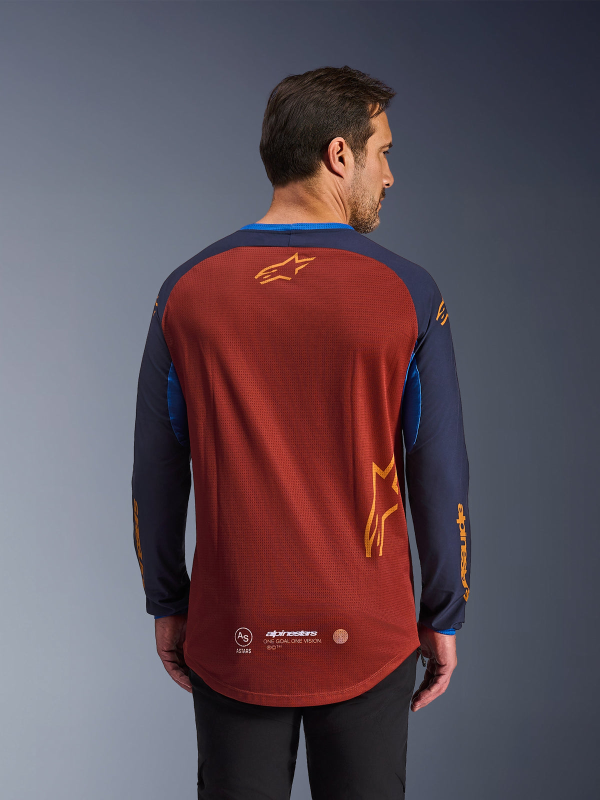 Alpinestars Maxdura Dual Jersey in Rust Brown en Mood Indigo, achteraanzicht, met een ademende mesh torso, donkerblauwe mouwen met oranje Alpinestars branding en een verlengde achterzoom voor extra dekking.