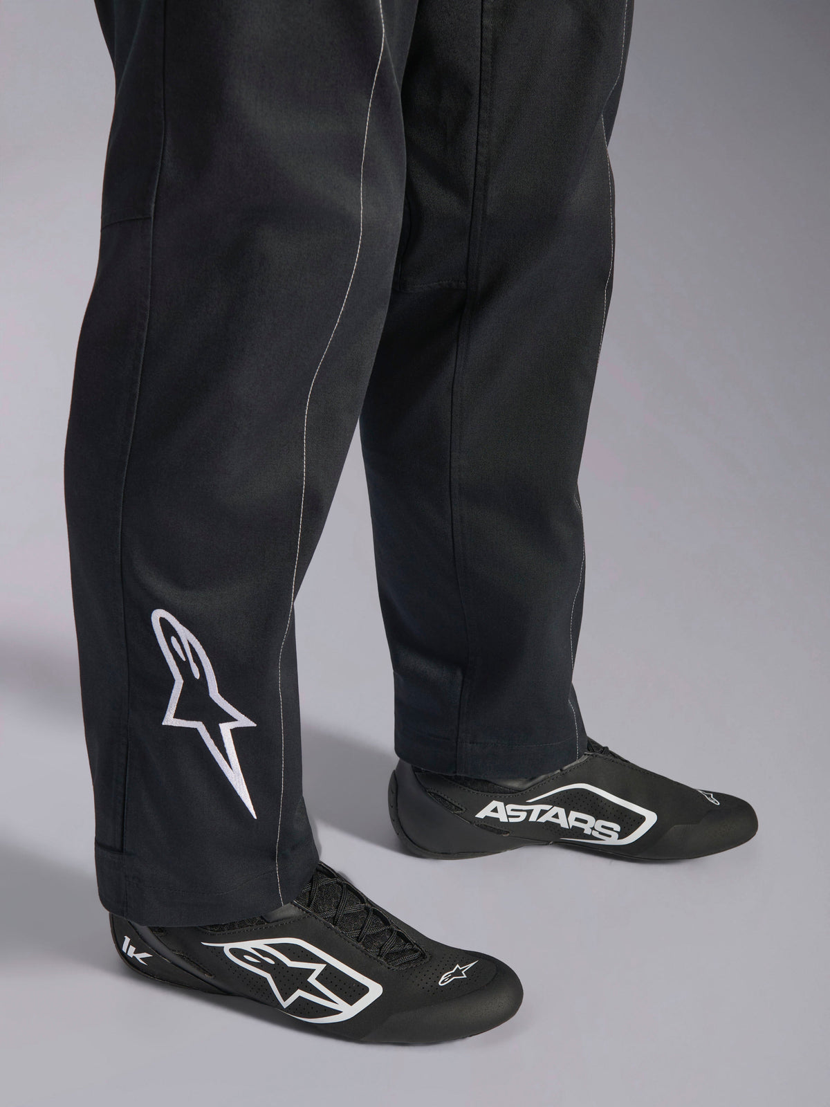 Alpinestars Kart Indoor V2 Pak, zwart kartingpak, close-up van de onderbenen en voeten met een wit Alpinestars-logo op de kuit, gedragen met bijpassende zwart-witte raceschoenen, ontworpen voor recreatief karten