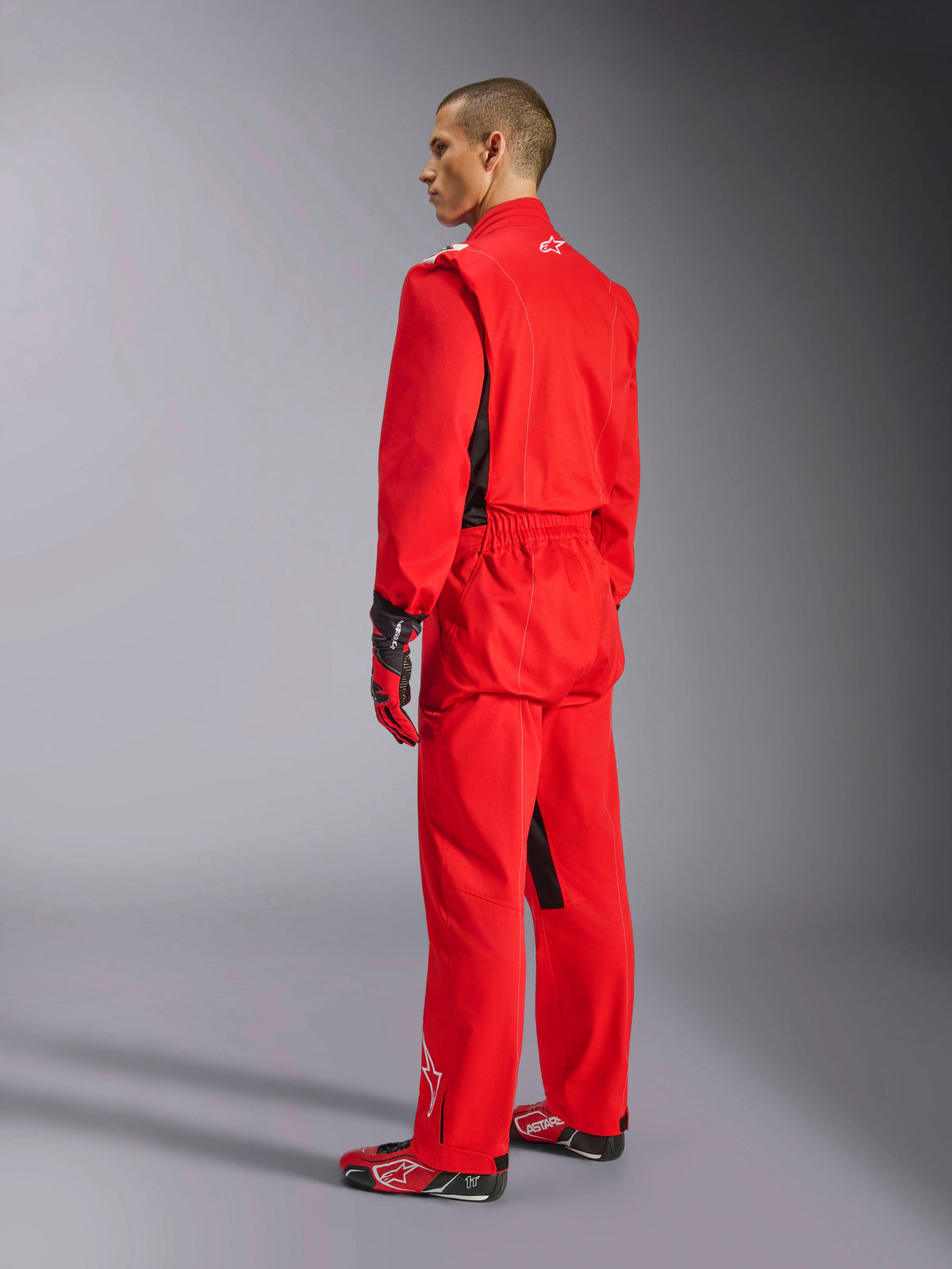 Alpinestars Kart Indoor V2 Suit, rood kartpak, driekwart achteraanzicht op een model, gedragen met bijpassende rode handschoenen en raceschoenen, enkellaagse poly-katoen keperconstructie, professionele motorsportuitrusting voor indoor karten