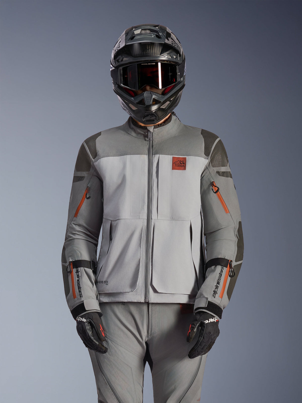 Alpinestars Nazca 3L GORE-TEX PRO Jacket, Adventure Motorcycle Jacket, Dark Gray and Mid Gray with orange zipper accents, worn with matching pants and black helmet, featuring durable textile construction with visible GORE-TEX PRO and All Terra branding