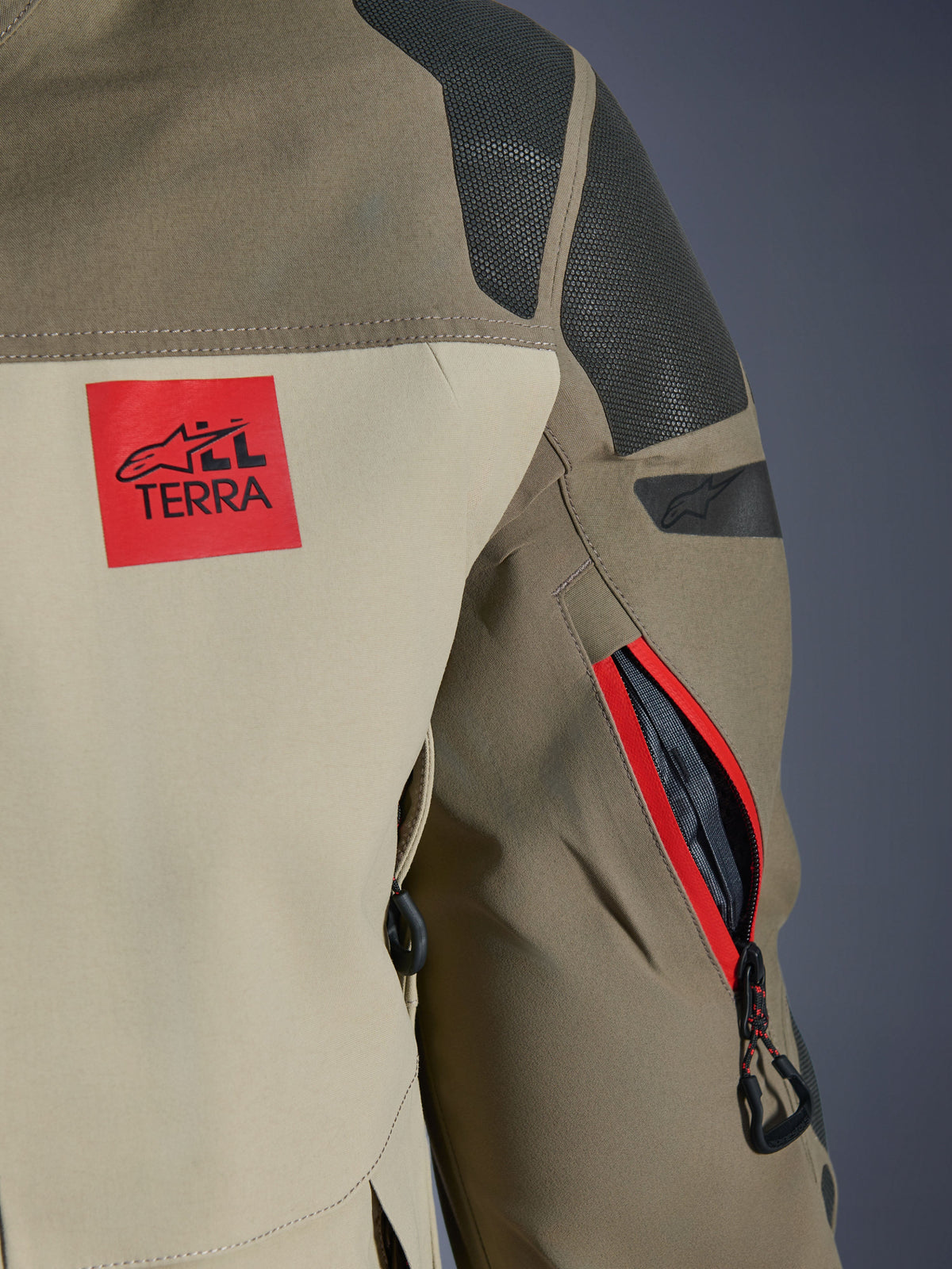 Alpinestars Nazca 3L GORE-TEX PRO Jas, Walnut Rock Brown, detail van de schouder en mouw aan de achterzijde, rode 'ALL TERRA' logopatch, getextureerde zwarte Superfabric schouderpanelen, ventilatieopening met rits op de arm met rode bies, premium avontuurlijke motorkleding
