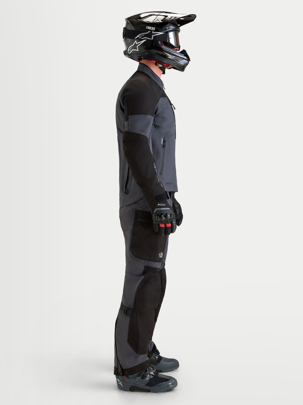 Alpinestars Arenis Gore-Tex jas, heren adventure touring motortextieljas in zwart en donkergrijs, zijaanzicht op een model met bijpassende uitrusting en helm, AA-gecertificeerde waterdichte all-terrain kleding