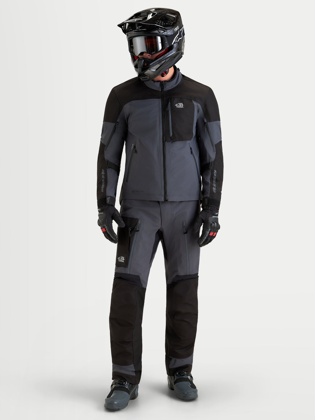 Alpinestars Arenis Gore-Tex jas, heren adventure motorjas in zwart en donkergrijs, gedragen door een rijder met bijpassende helm en beschermende uitrusting, volledig vooraanzicht