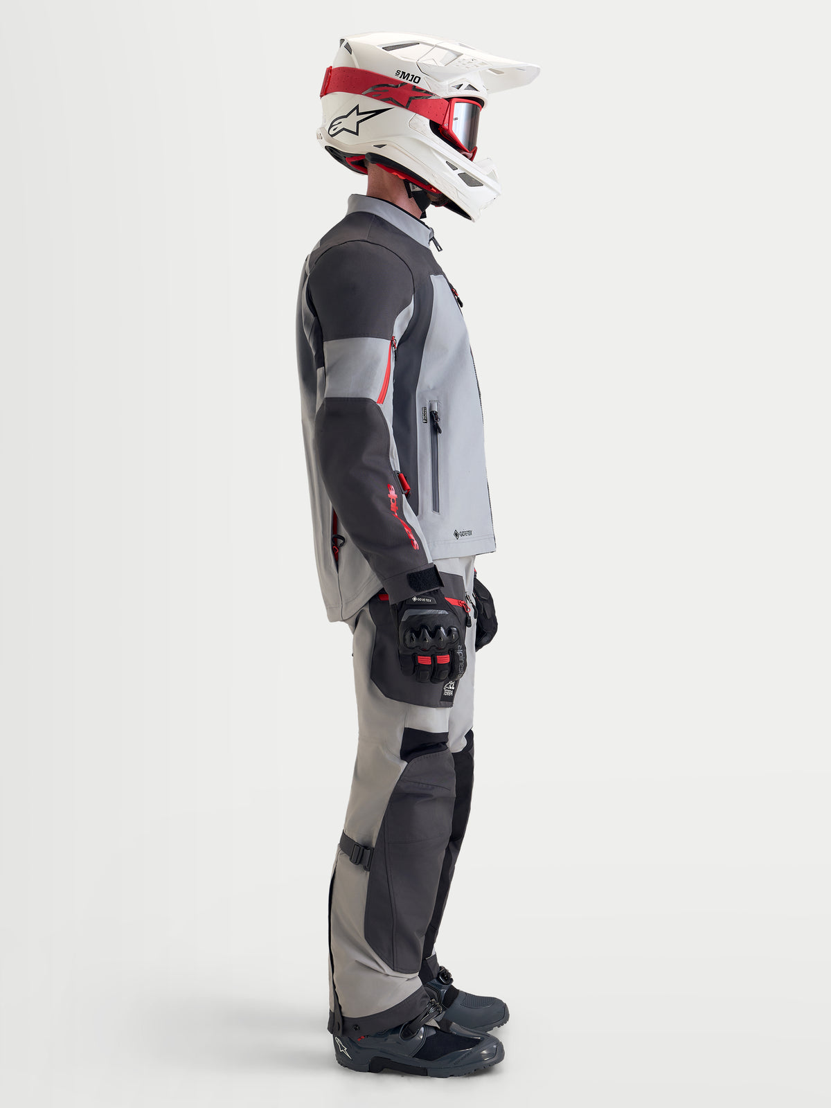 Alpinestars Arenis Gore-Tex uitrustingsset, adventure-motorjas en -broek voor heren in grijs en zwart, zijaanzicht op model met bijpassende uitrusting en helm, waterdichte all-terrain motorkleding
