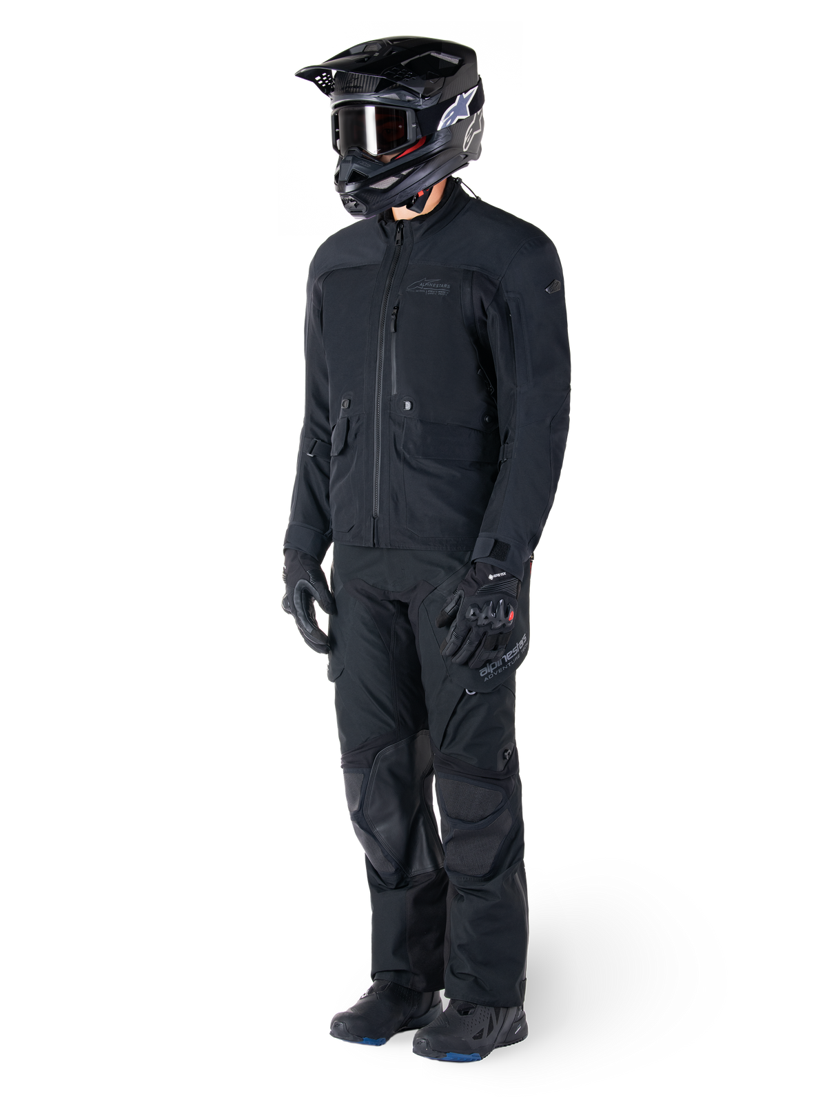 Motorrijder die de Alpinestars St-7 Prime GORE-TEX jas in het zwart draagt, gecoördineerde adventure touring-outfit met bijpassende zwarte broek, zwarte helm met bril en handschoenen, met een gestroomlijnd en functioneel ontwerp voor prestaties onder alle weersomstandigheden.