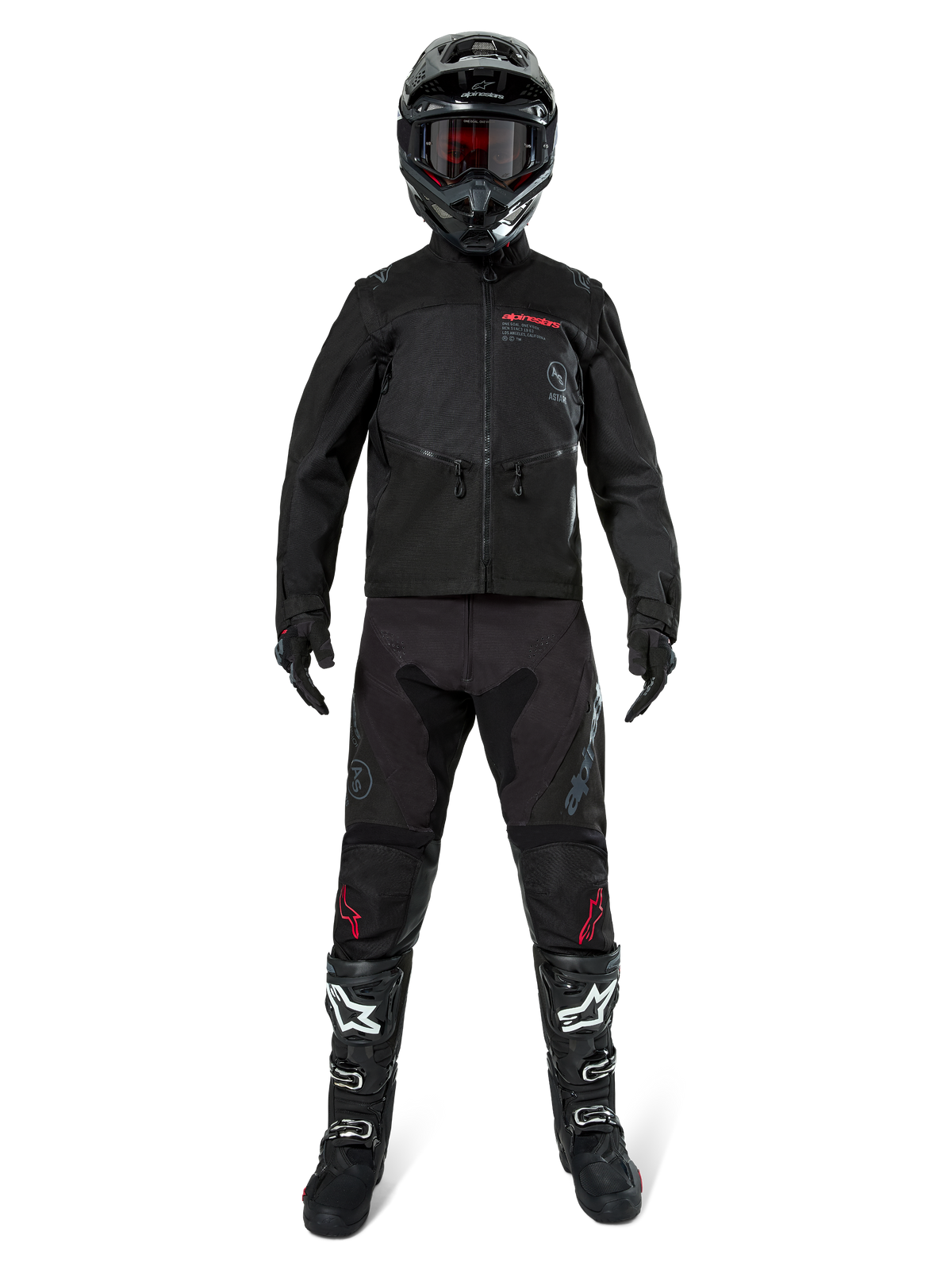Alpinestars Pro-Dura Jas, zwarte off-road enduro jas, getoond op een model met een volledige uitrusting inclusief zwarte helm met rode bril, zwarte broek met rode accenten, zwart-witte laarzen en zwarte handschoenen, rally-geïnspireerd robuust ontwerp voor trailrijden