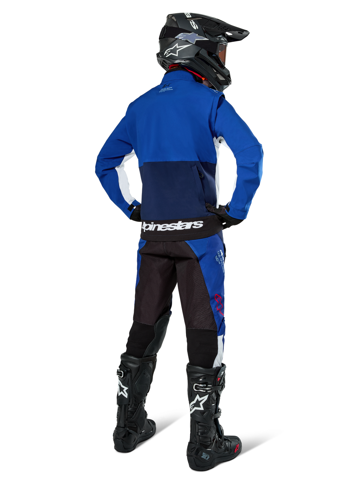 Motocrossrijder van achteren gezien die de Alpinestars Lite-Dura Softshell Jas in Navy Bright Blue en wit draagt, gecombineerd met bijpassende endurobroek, zwarte helm en zwarte laarzen, complete off-road race-uitrusting