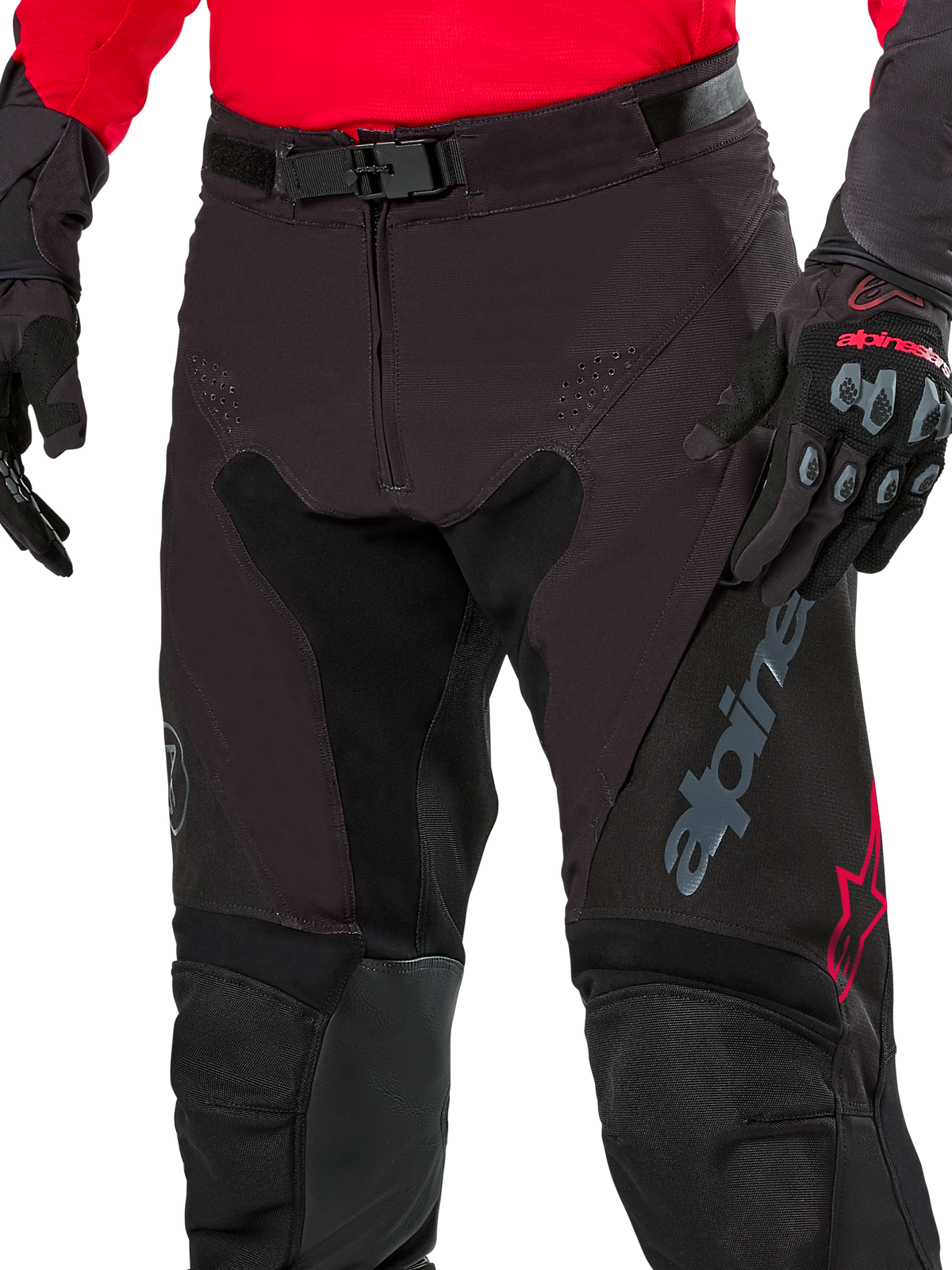Close-up van Alpinestars Pro-Dura broek, endurobroek, Black Magnet White met rode accenten, voorzien van een veilige magnetische gespsluiting en ritssluiting, gedragen met bijpassende rode jersey en zwarte handschoenen, duurzame ripstop-constructie voor off-road rijden